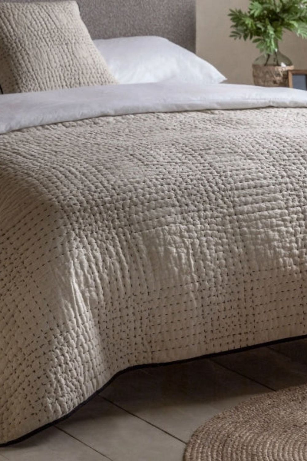 lifestyle image of a beige bedspread with a black trim
