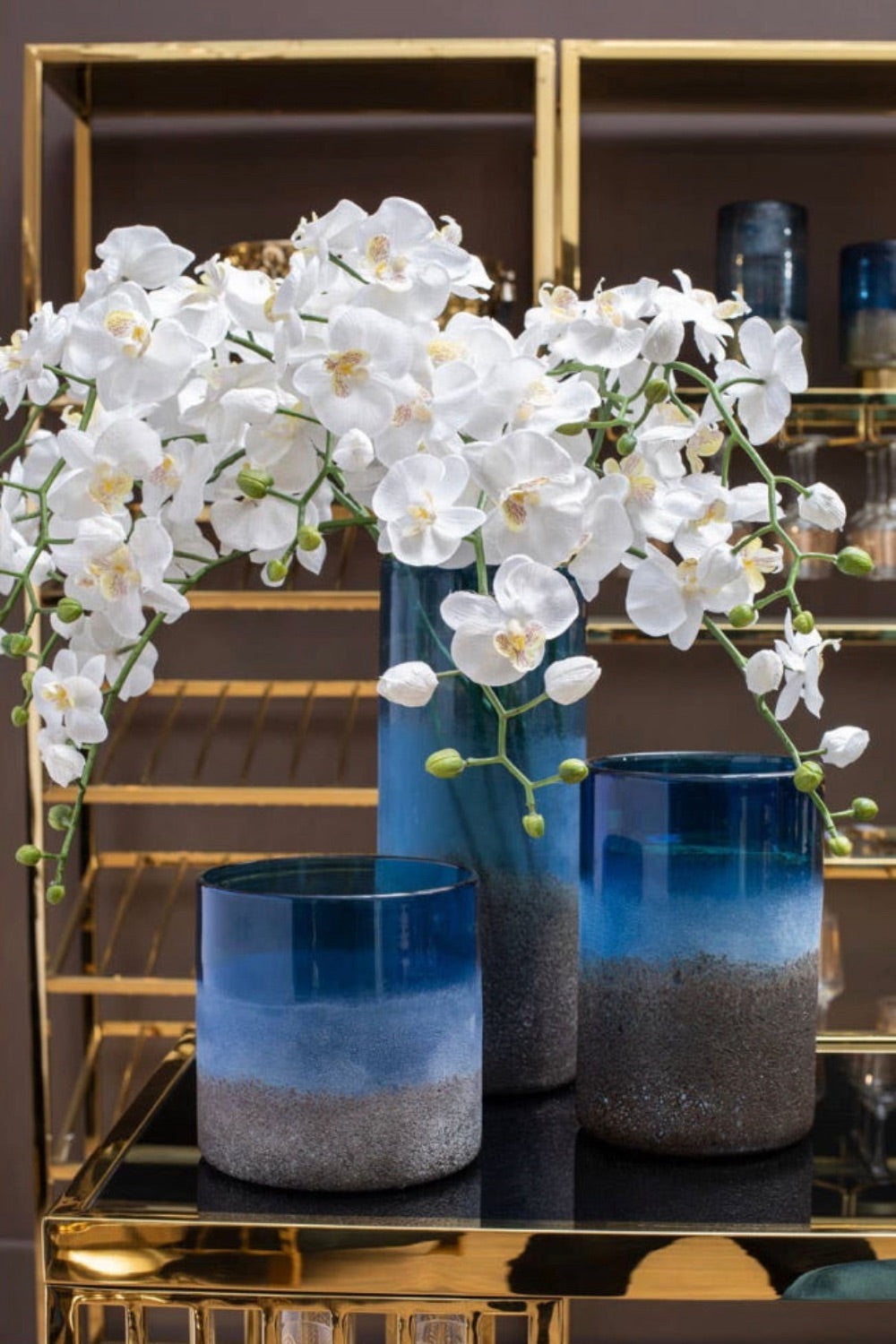 White flowers in a coastal inspired blue textured glass vase on a reflective surface with a gold frame background