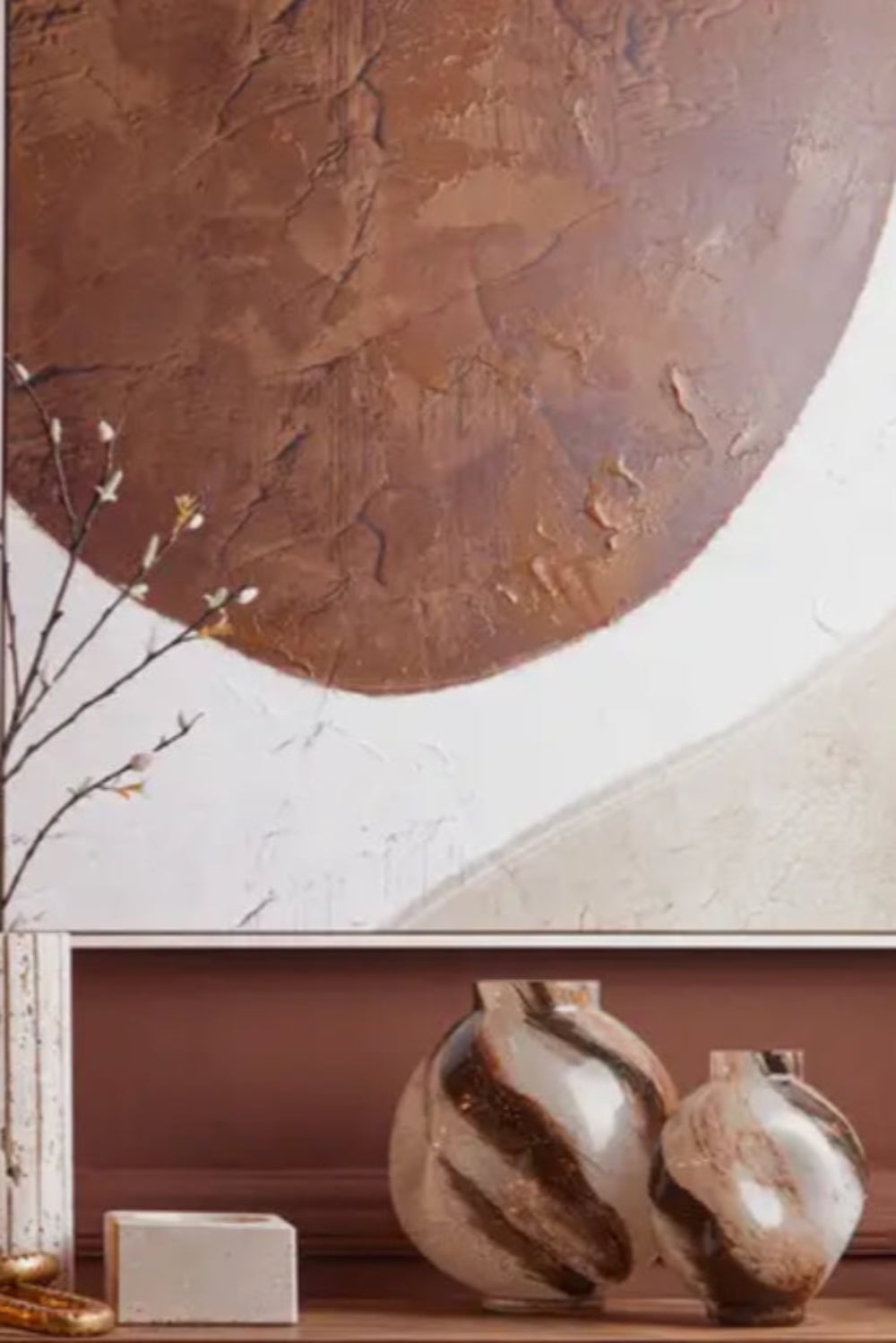 Decorative wall art with a textured brown circle and two mocha swirl glass vases on a table