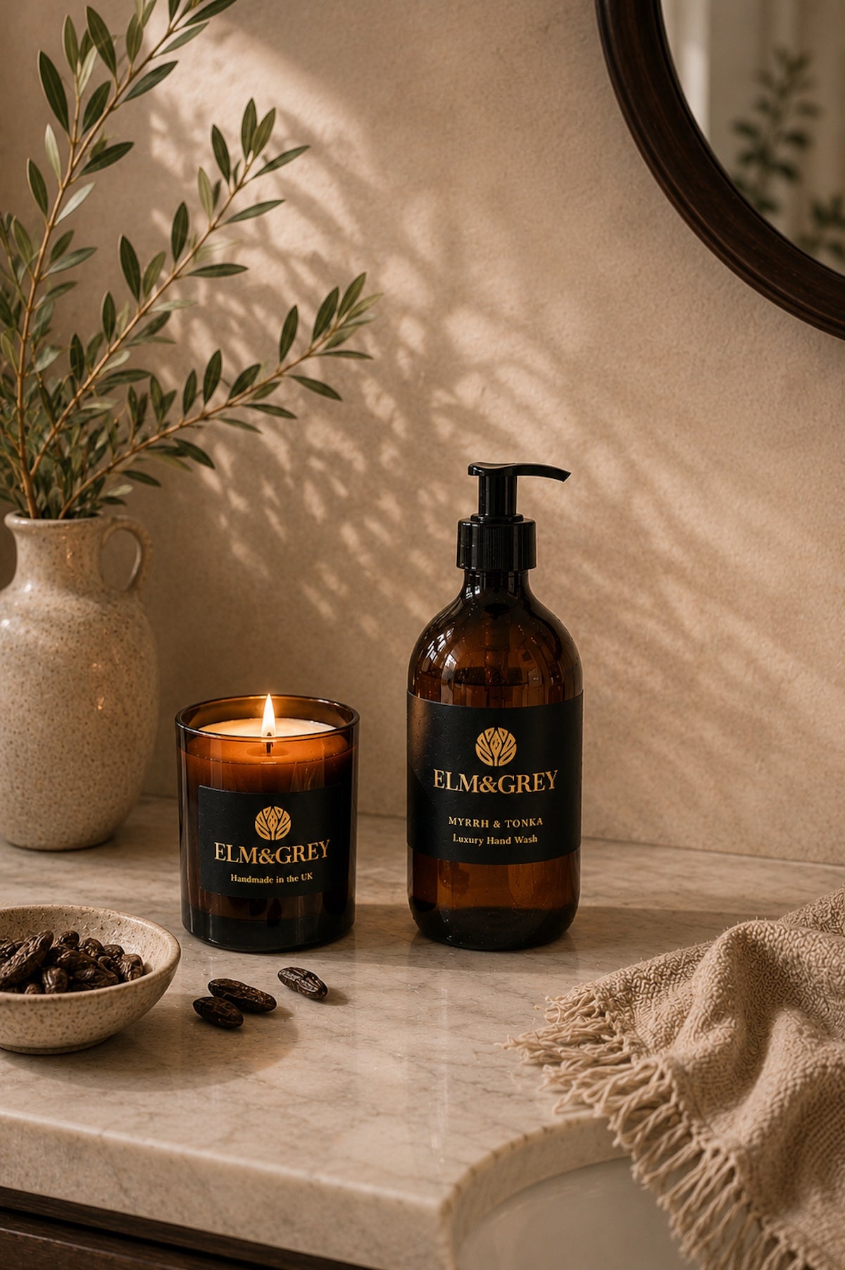 Elm & Grey Myrrh and Tonka luxury hand wash on a marble bathroom surface with a lit candle and
olive branches in warm candlelight