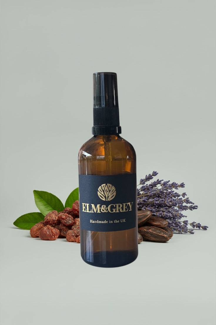 Amber bottle with black cap labeled 'Elm & Grey' on a light grey background with green leaves and lavender.