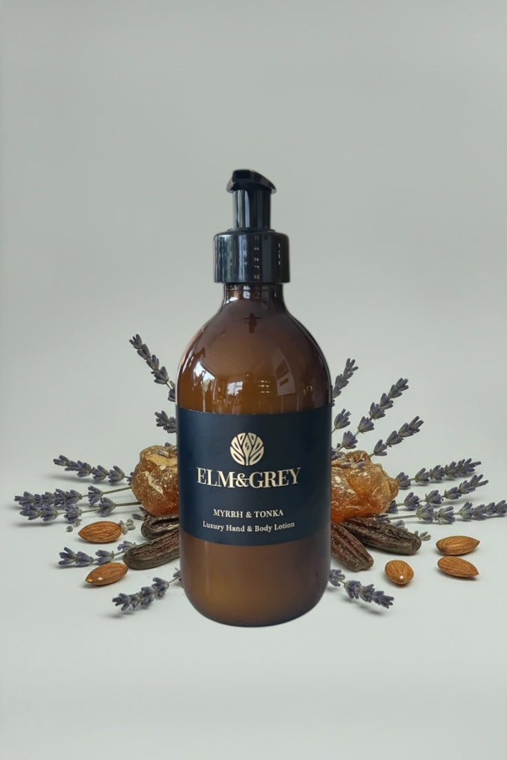 Amber bottle with black pump labeled 'Elm & Grey' on a light grey background with dried lavender and almonds.