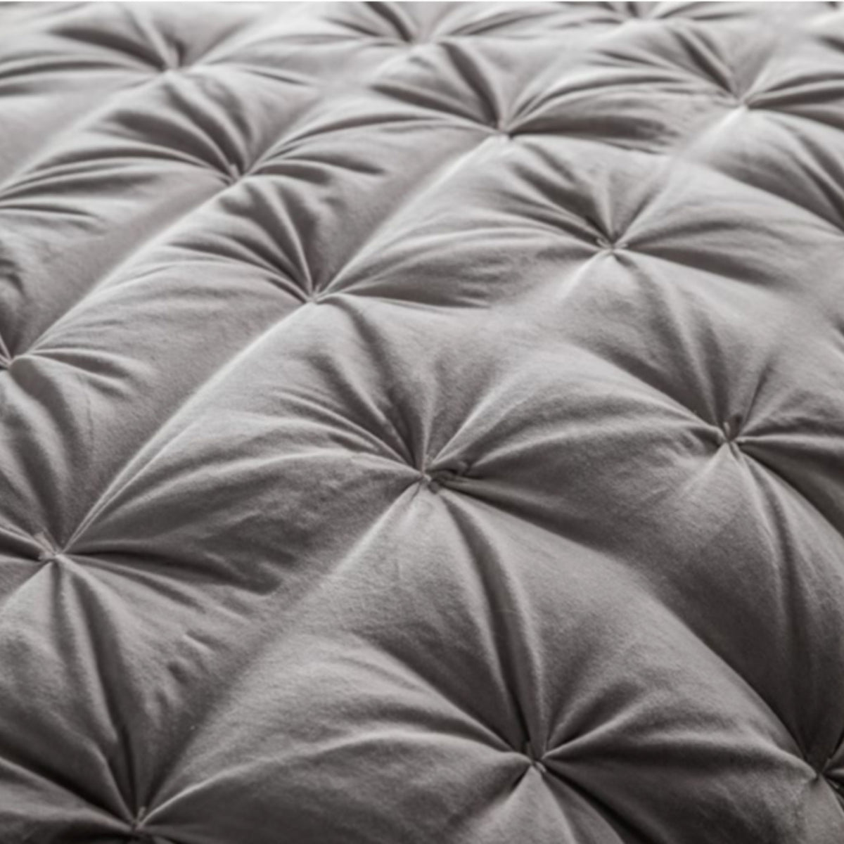Close-up of a grey quilted mattress pad with tufted design.