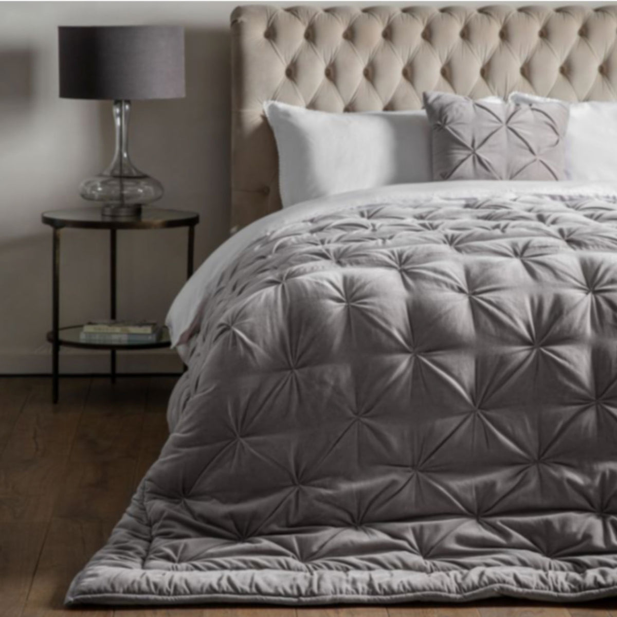 Grey quilted comforter on a bed with a tufted headboard and side table.