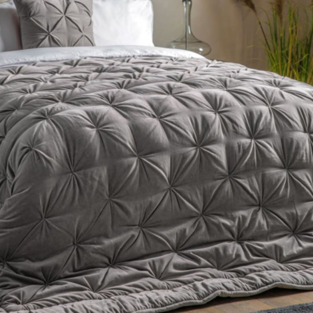 Grey quilted comforter on a bed with pillows and a plant in the background