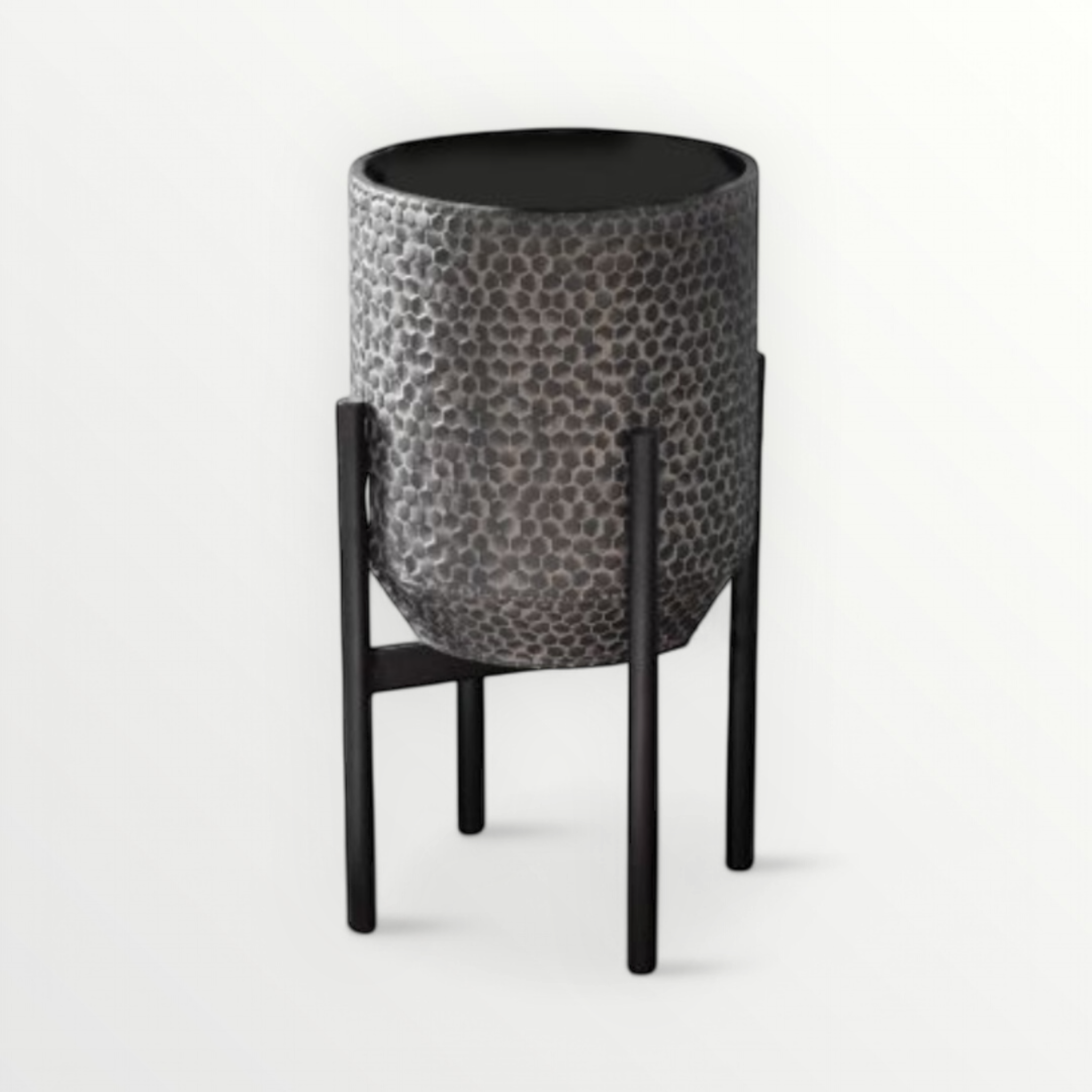 A small black textured metal planter with a honeycomb design on the pot, placed on a sleek black four-legged metal base.