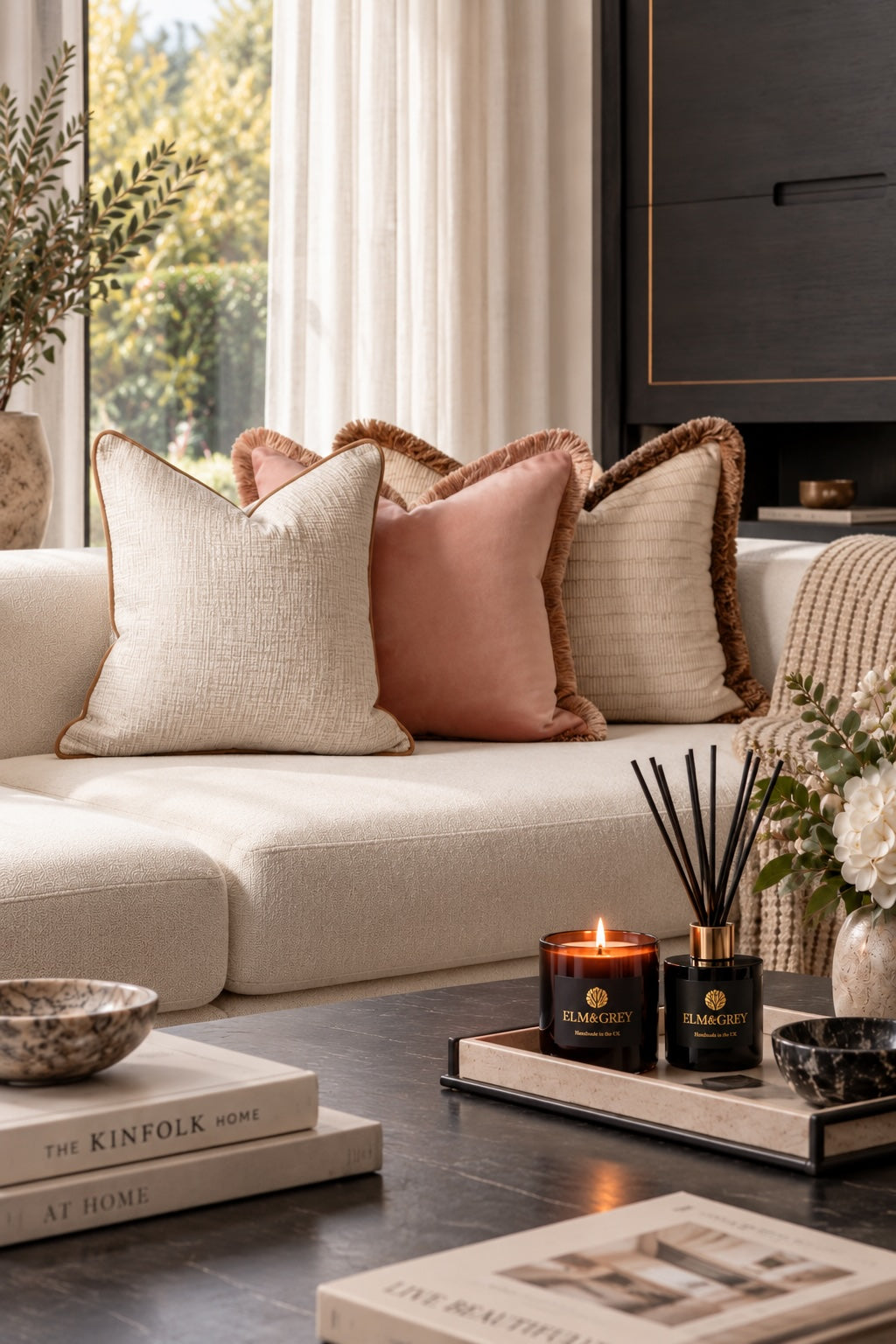 Champagne, Bracken and Pearl curated cushion trio styled on a cream sofa with Elm & Grey candle and diffuser in a warm neutral living room.
