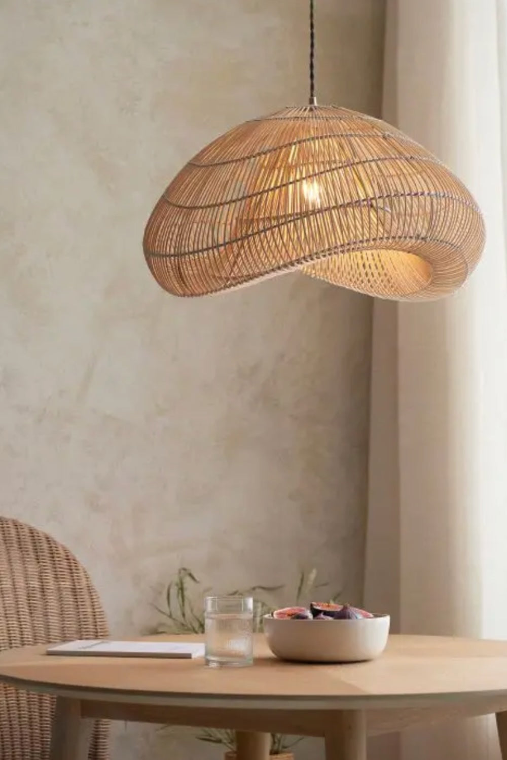 Woven pendant light hanging above a dining table with a neutral background. Elm & Grey.