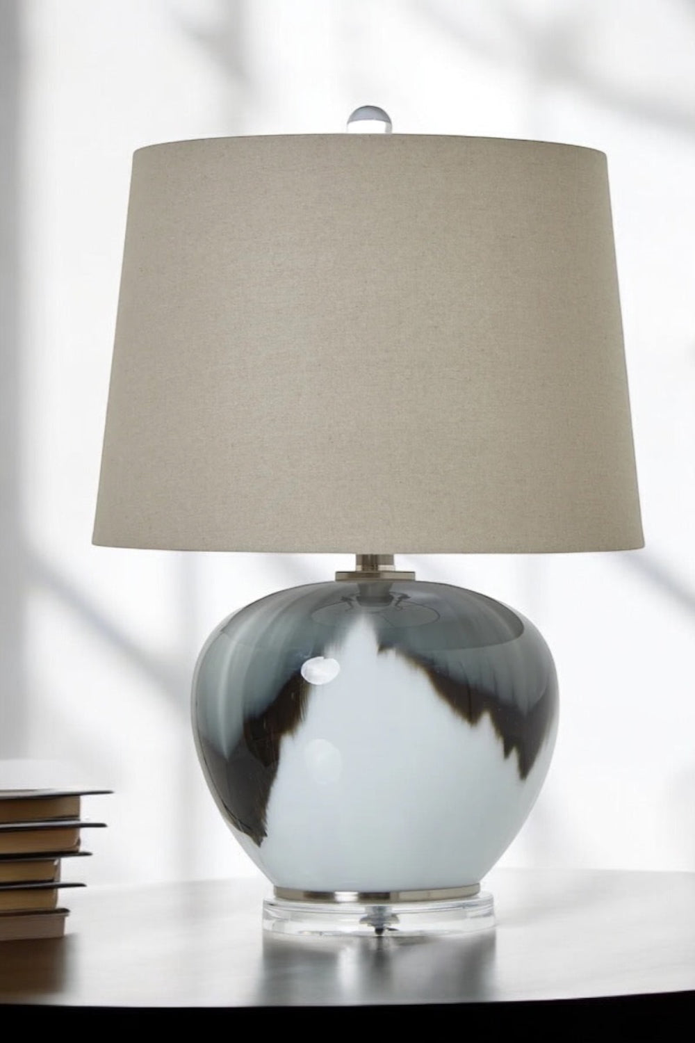 Table lamp with a grey and white marbled base and beige lampshade on a reflective surface, Elm & Grey.