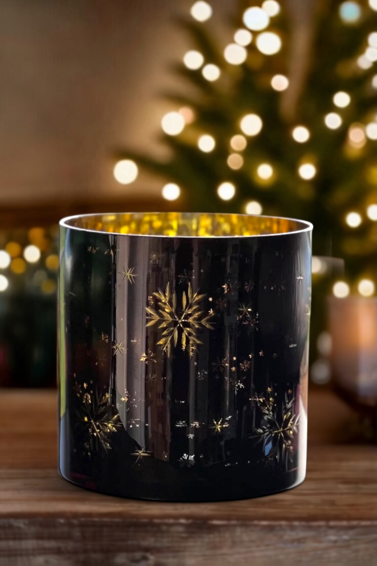 Navy candle holder with gold snowflake design in front of a Christmas tree with lights.