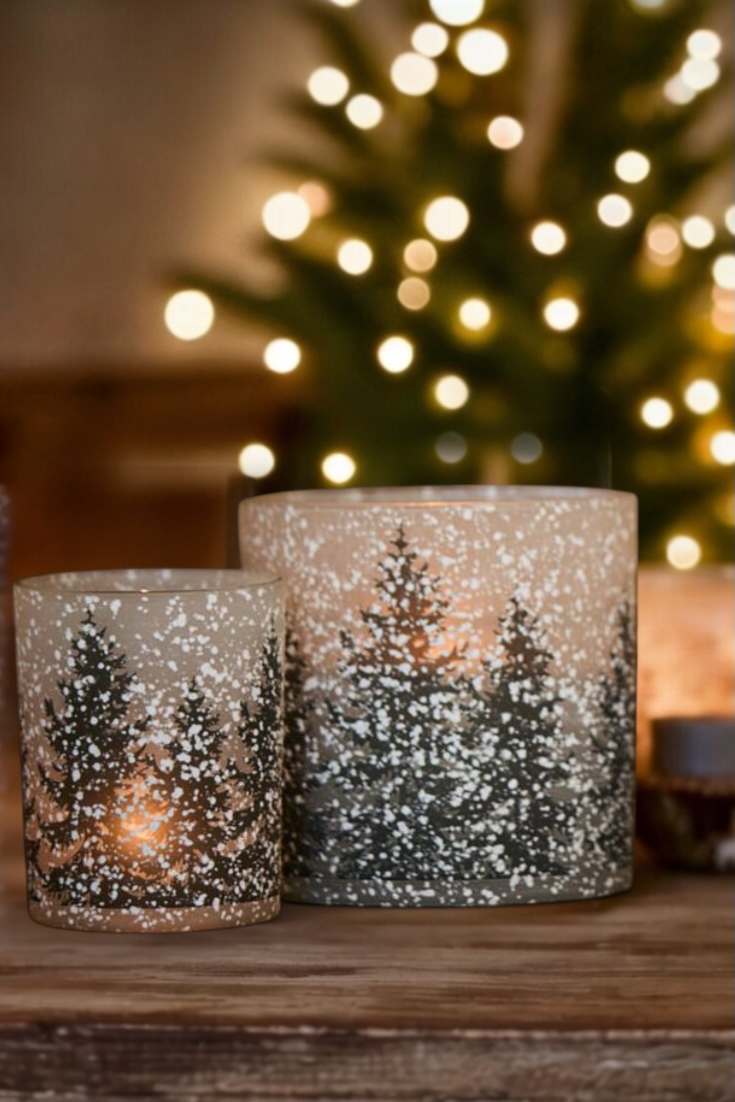 Two snowflake-patterned candles on a wooden surface with a blurred Christmas tree in the background.
