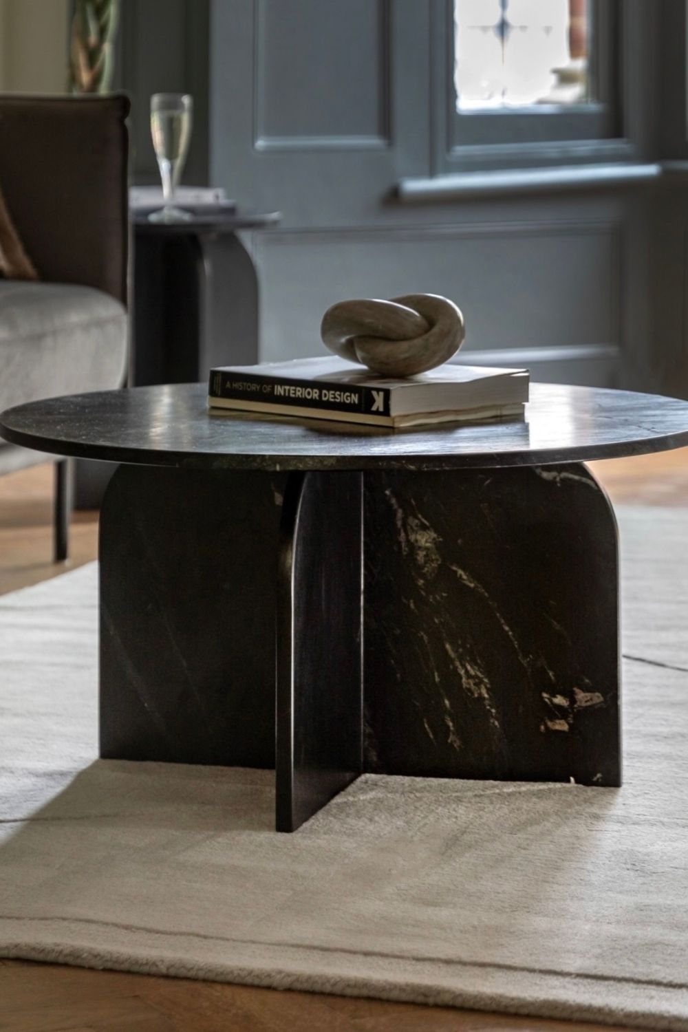 Modern black marble coffee table with books and a sculpture in a living room setting.
