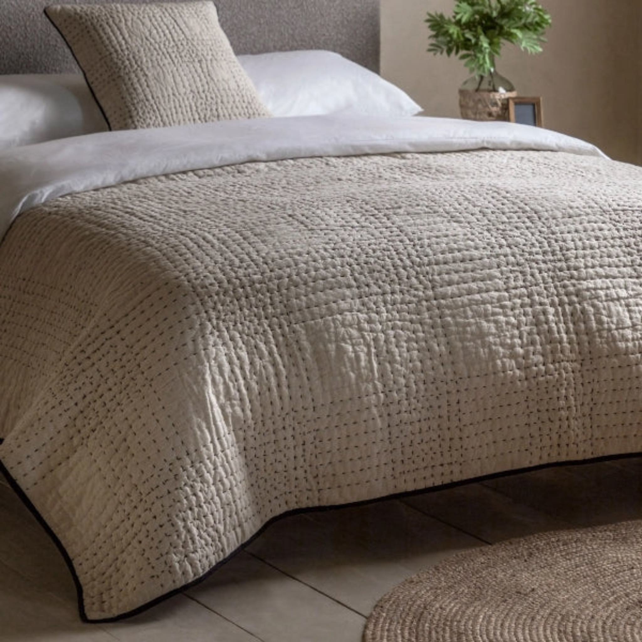 Textured beige blanket on a bed with pillows and a plant in the background