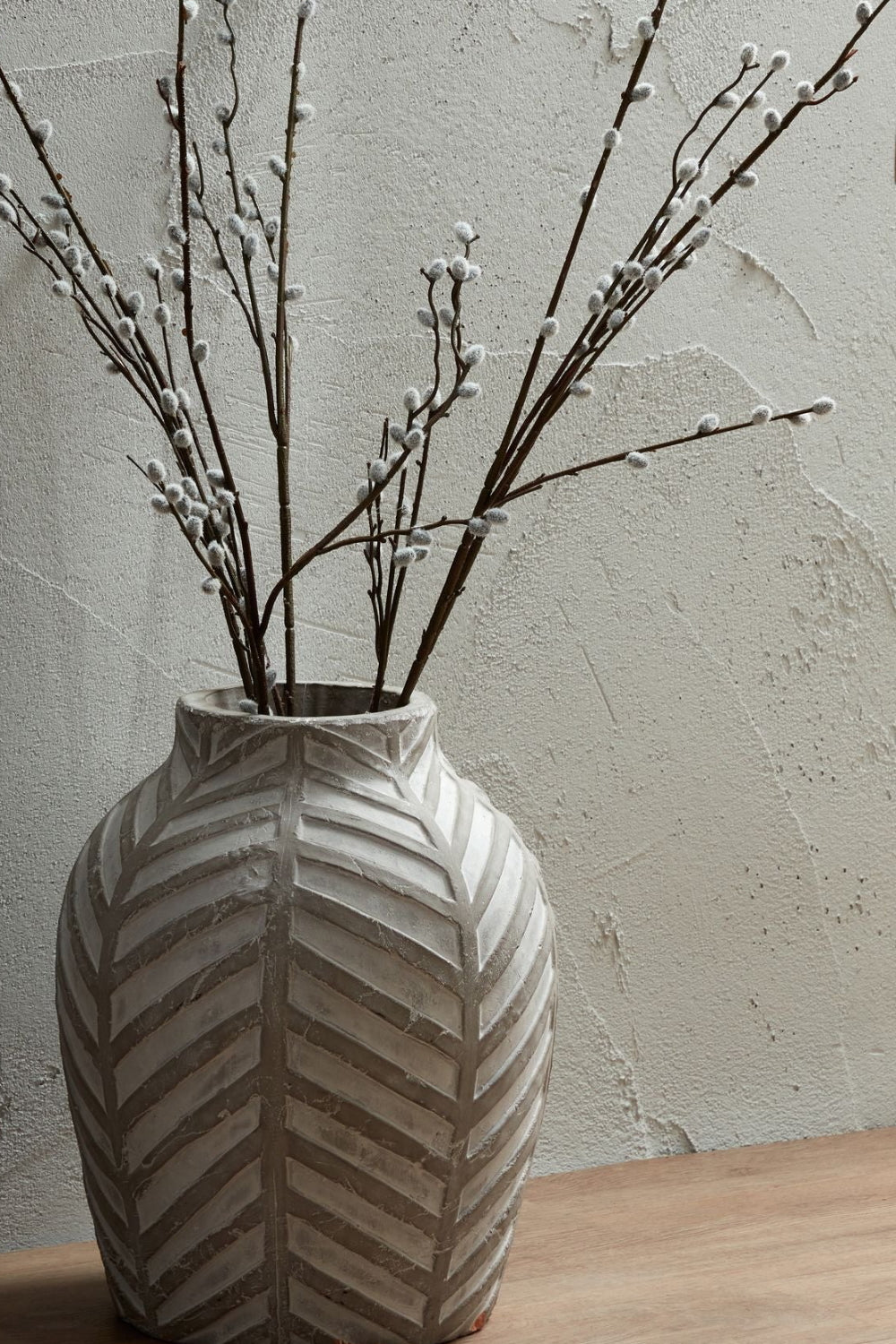 Vase with chevron pattern on a wooden surface against a textured wall.