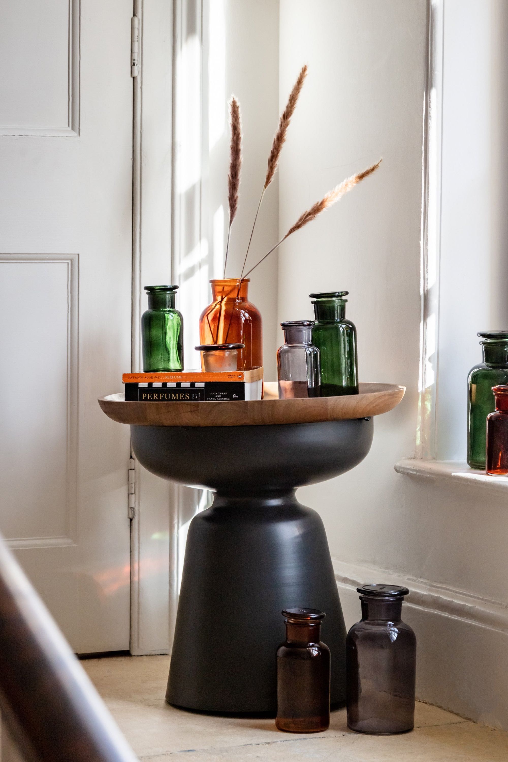 Decorative table with various coloured apothecary glass bottles against a neutral wall.