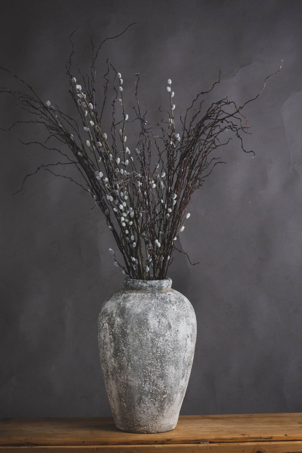 Decorative vase with willow branches on a wooden surface against a gray background