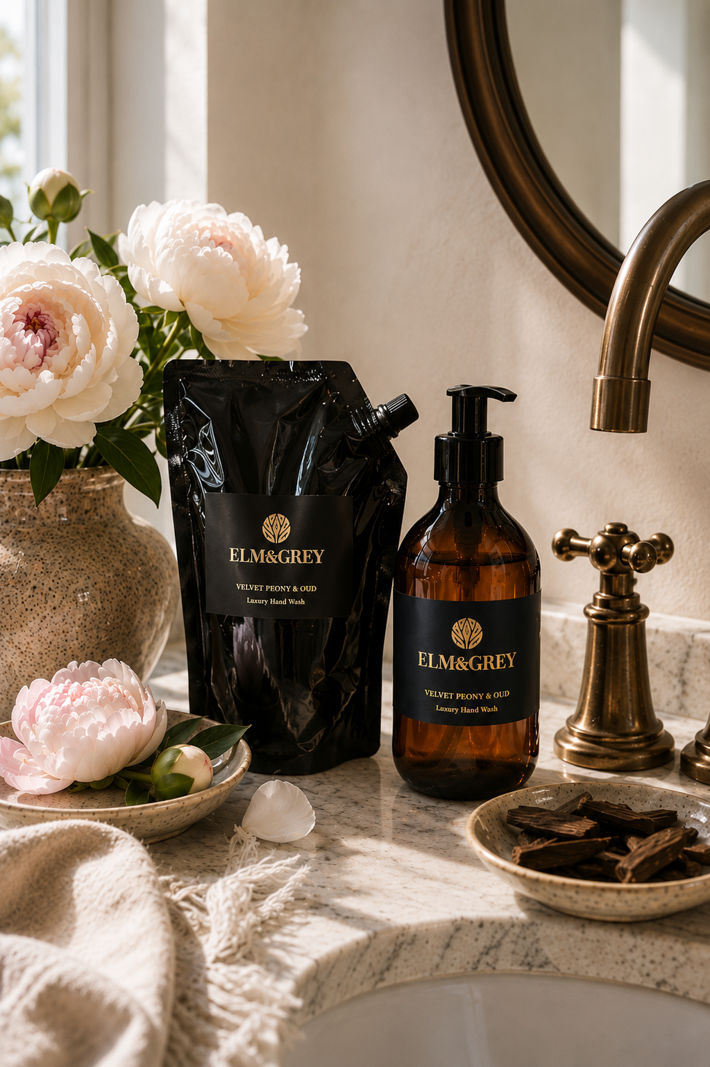 Velvet peony and oud hand and body wash bottle and refill pouch next to a sink styled with flowers and botanicals