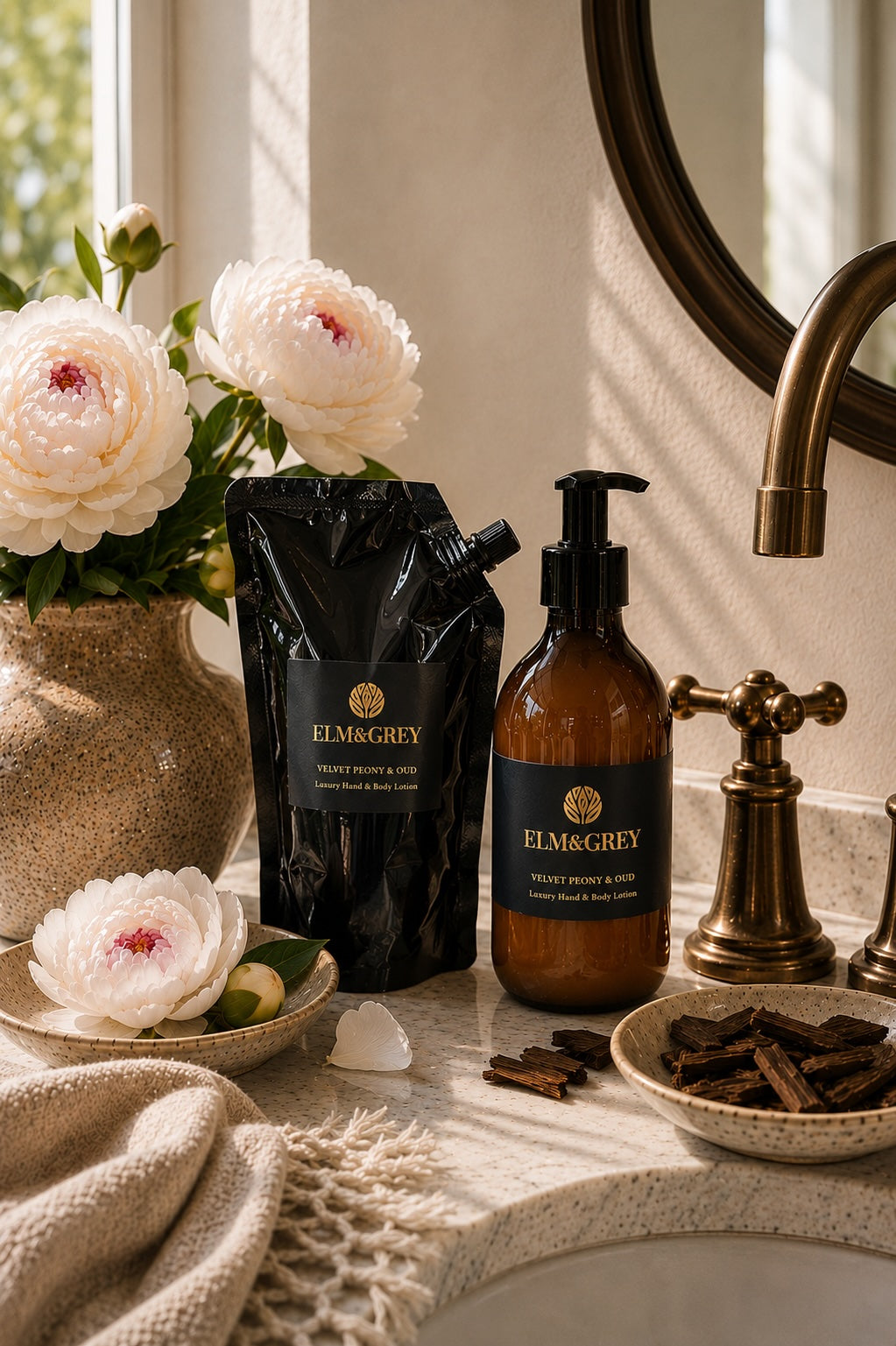 Velvet peony and oud hand and body lotion refill pouch and bottle styled next to a luxury marble bathroom sink with flowers and botanicals.