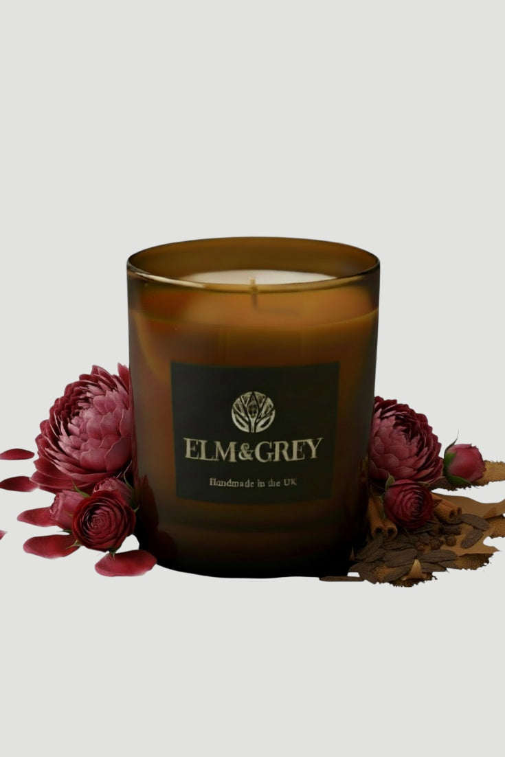 Brown candle with 'ELM&GREY' branding surrounded by red flowers on a light gray background