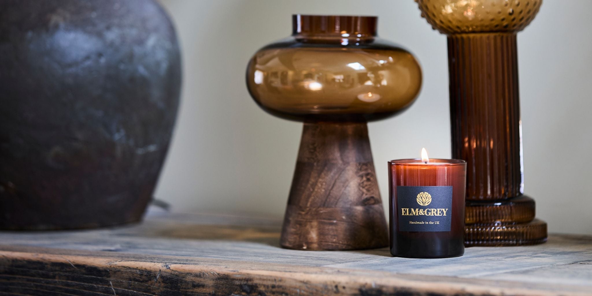 elm and grey larger amber candle lit on a sideboard wtih amber glass and wooden decorative accessories