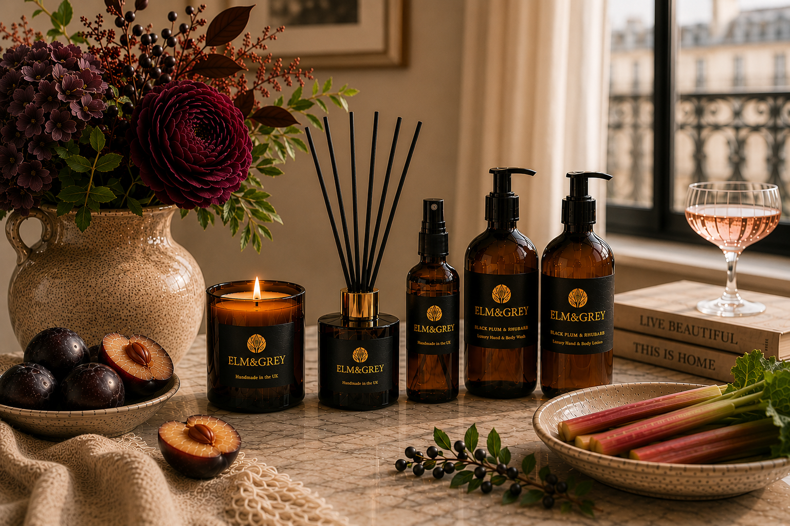 Elm & Grey Black Plum & Rhubarb luxury home fragrance collection featuring scented candle, reed diffuser, room spray, hand wash and body lotion styled with ripe plums and rhubarb in a warm sunlit interior.