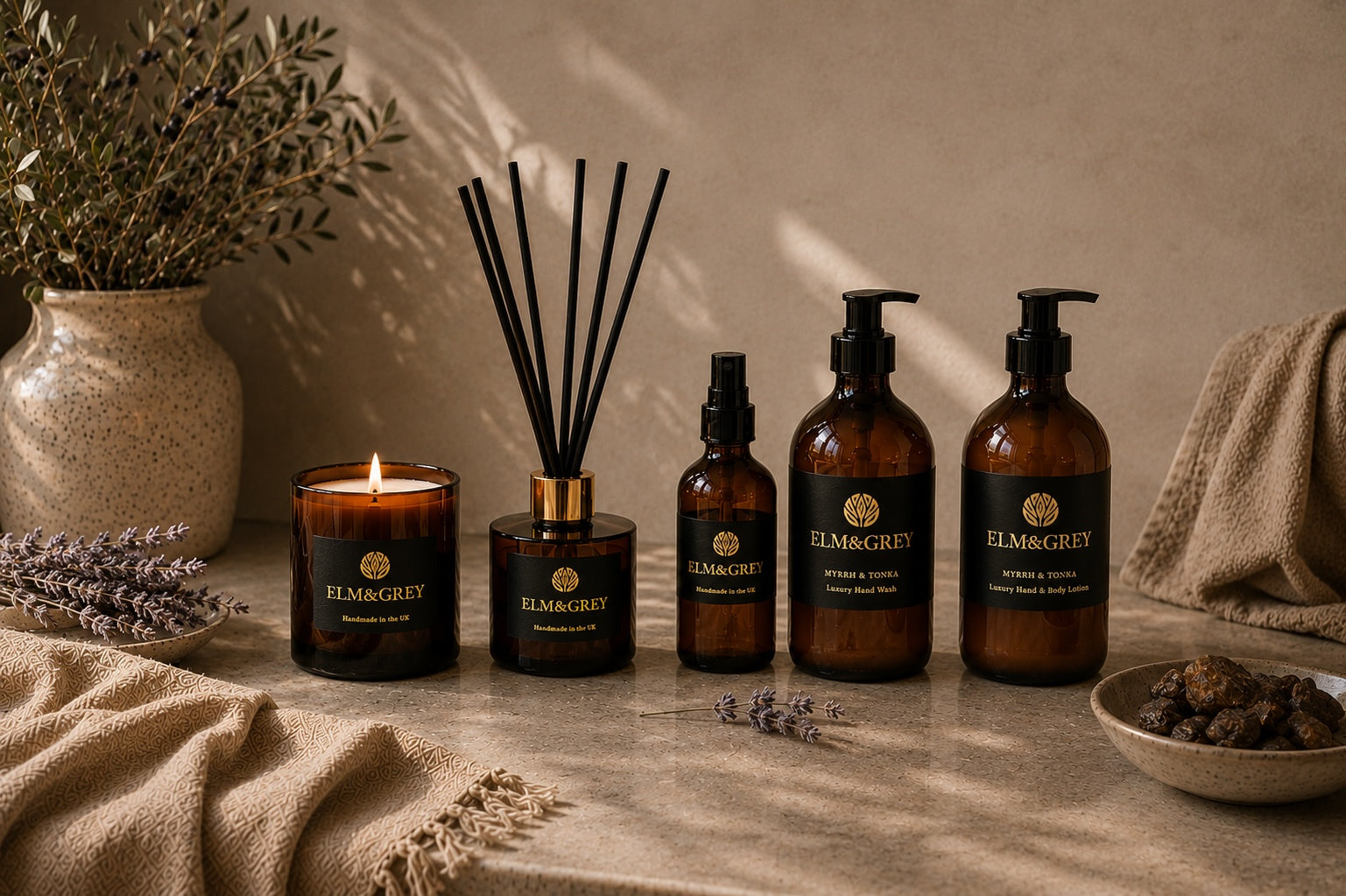 Elm & Grey Myrrh & Tonka luxury home fragrance collection featuring scented candle, reed diffuser, room spray, hand wash and hand & body lotion styled on a stone surface with warm neutral décor and soft natural light.