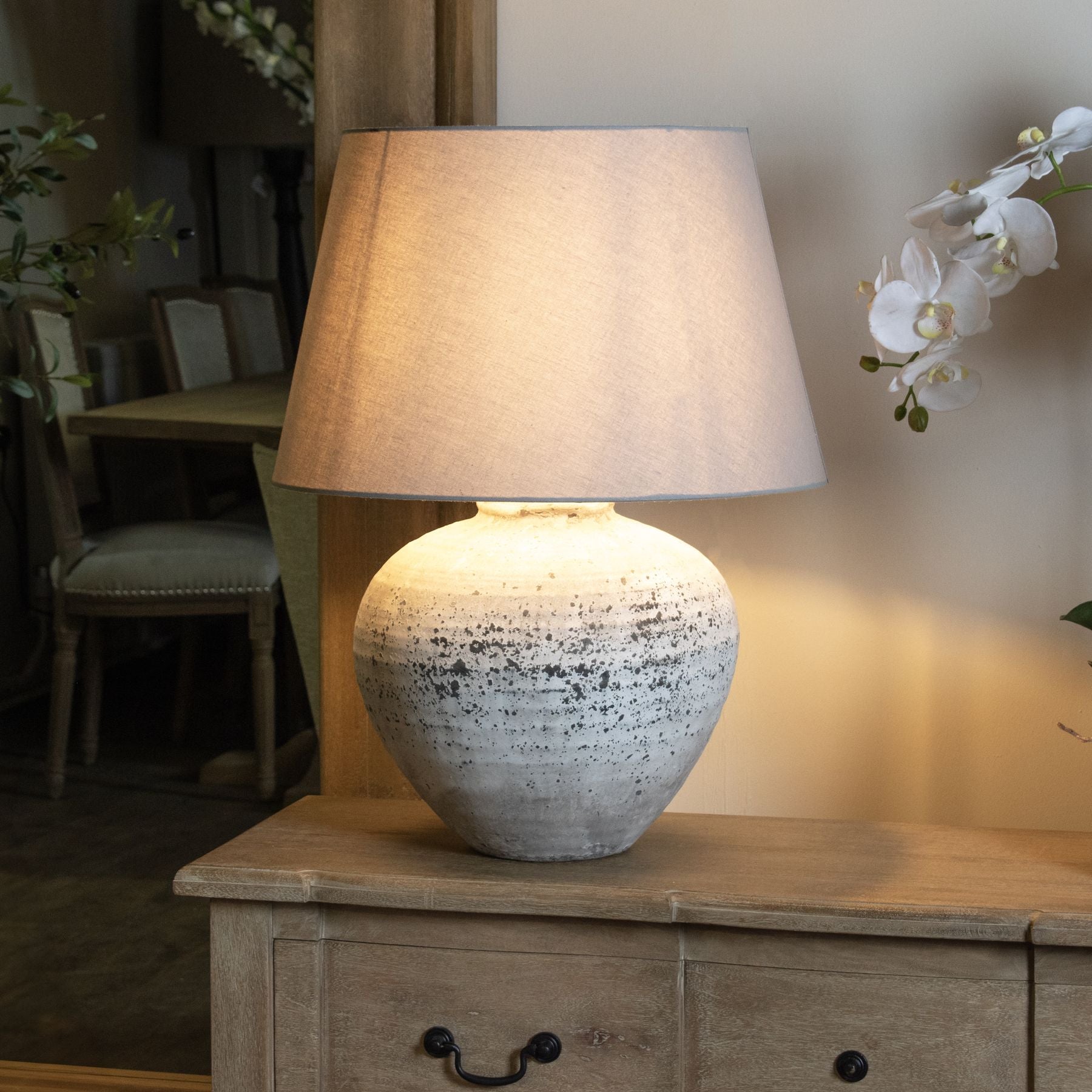 A ceramic table lamp with a textured stone effect and a light grey fabric shade, placed on a wooden side table.