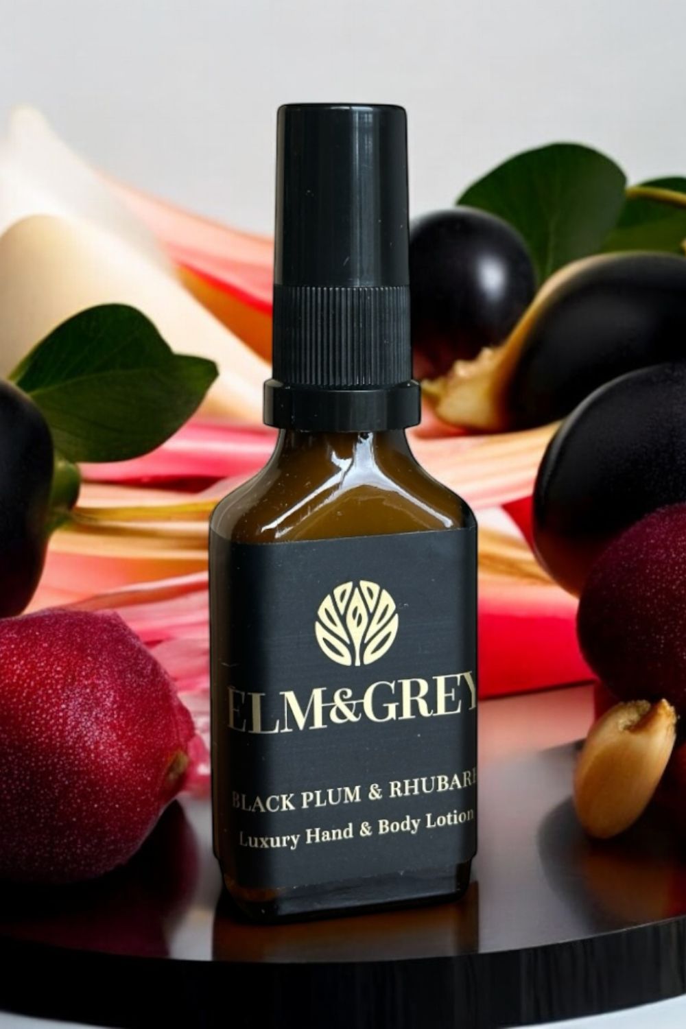 Bottle of Elm & Grey Black Plum & Rhubarb luxury hand & body lotion with fruits in the background