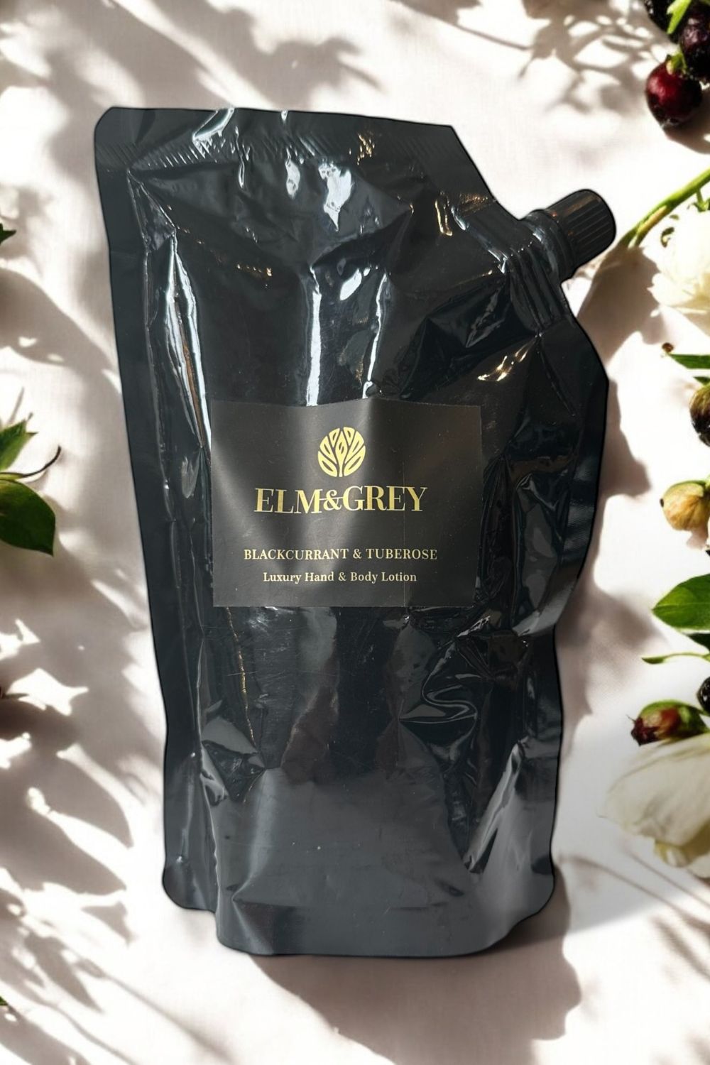 Black refill pouch lotion with 'Elm & Grey' branding on a light background with flowers.