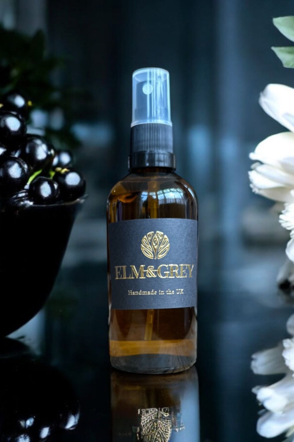 Bottle of Elm & Grey room spray on a reflective surface with blurred background