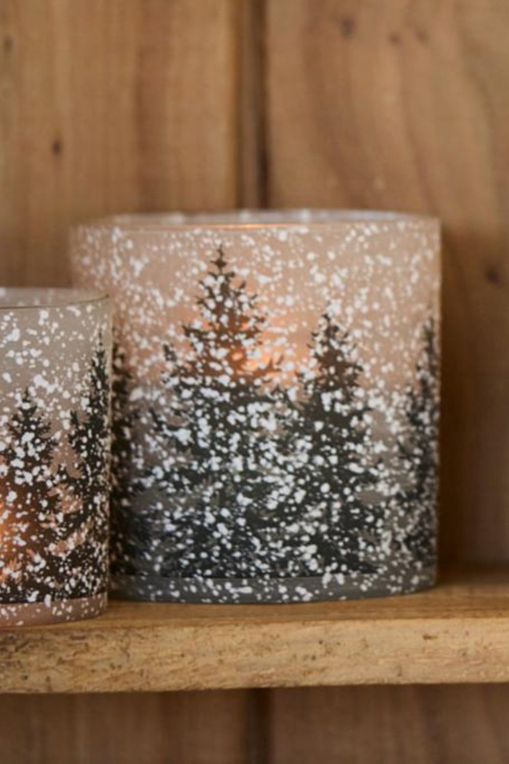 Two candle holders with winter scene design on a wooden shelf
