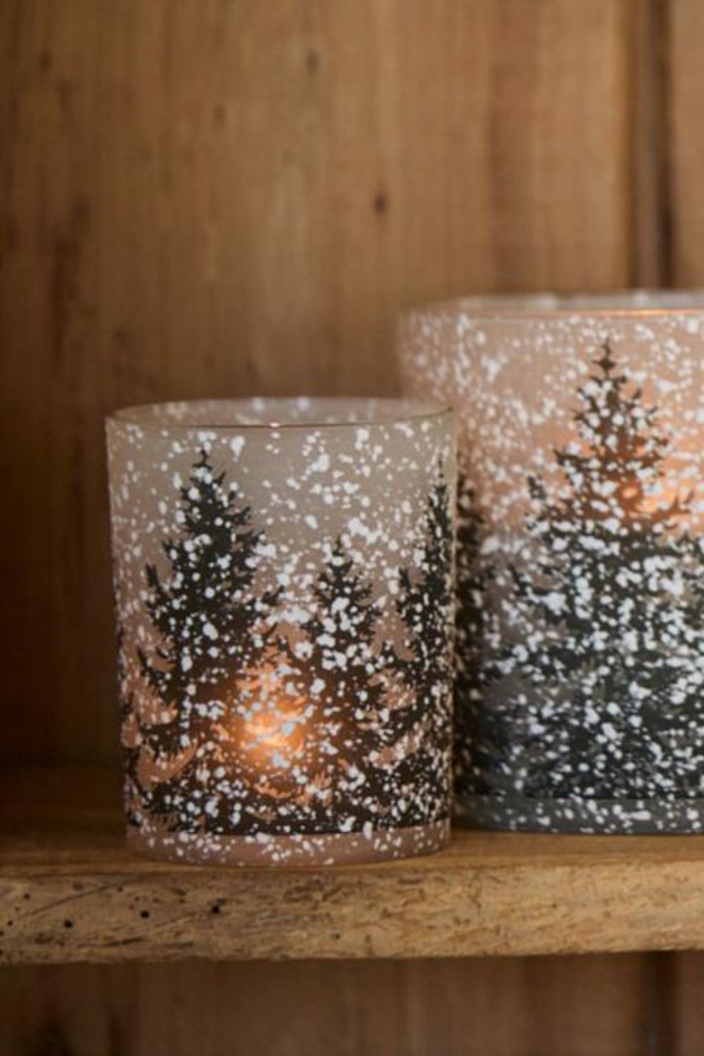 Two decorative candle holders with winter scene design on a wooden surface.