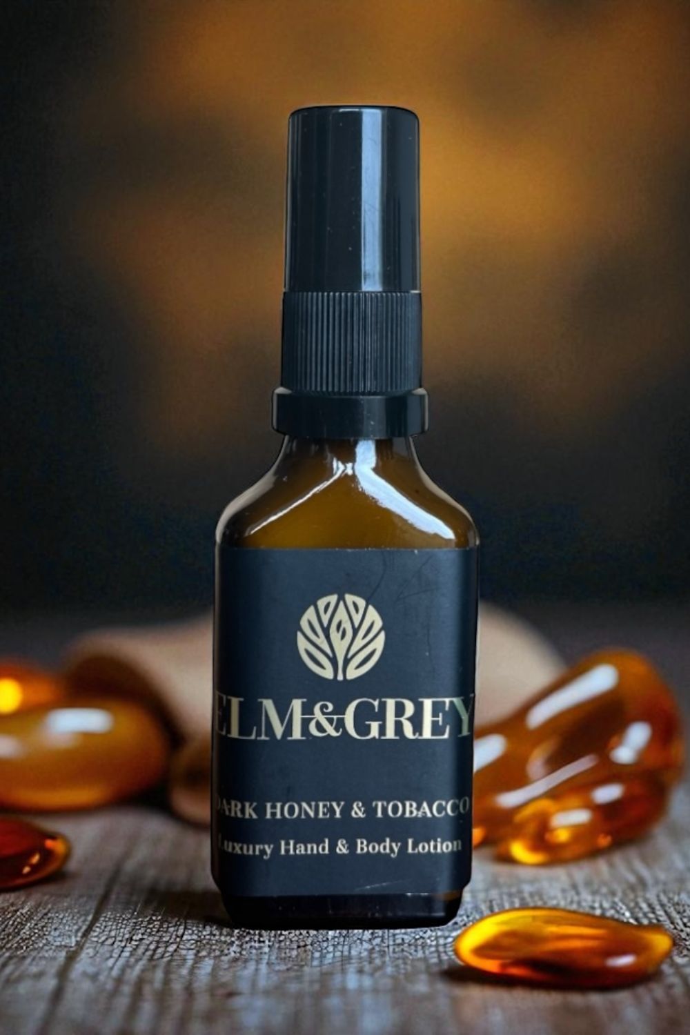 Bottle of elm and grey dark honey & tobacco luxury hand & body lotion on a wooden surface with amber glass stones.