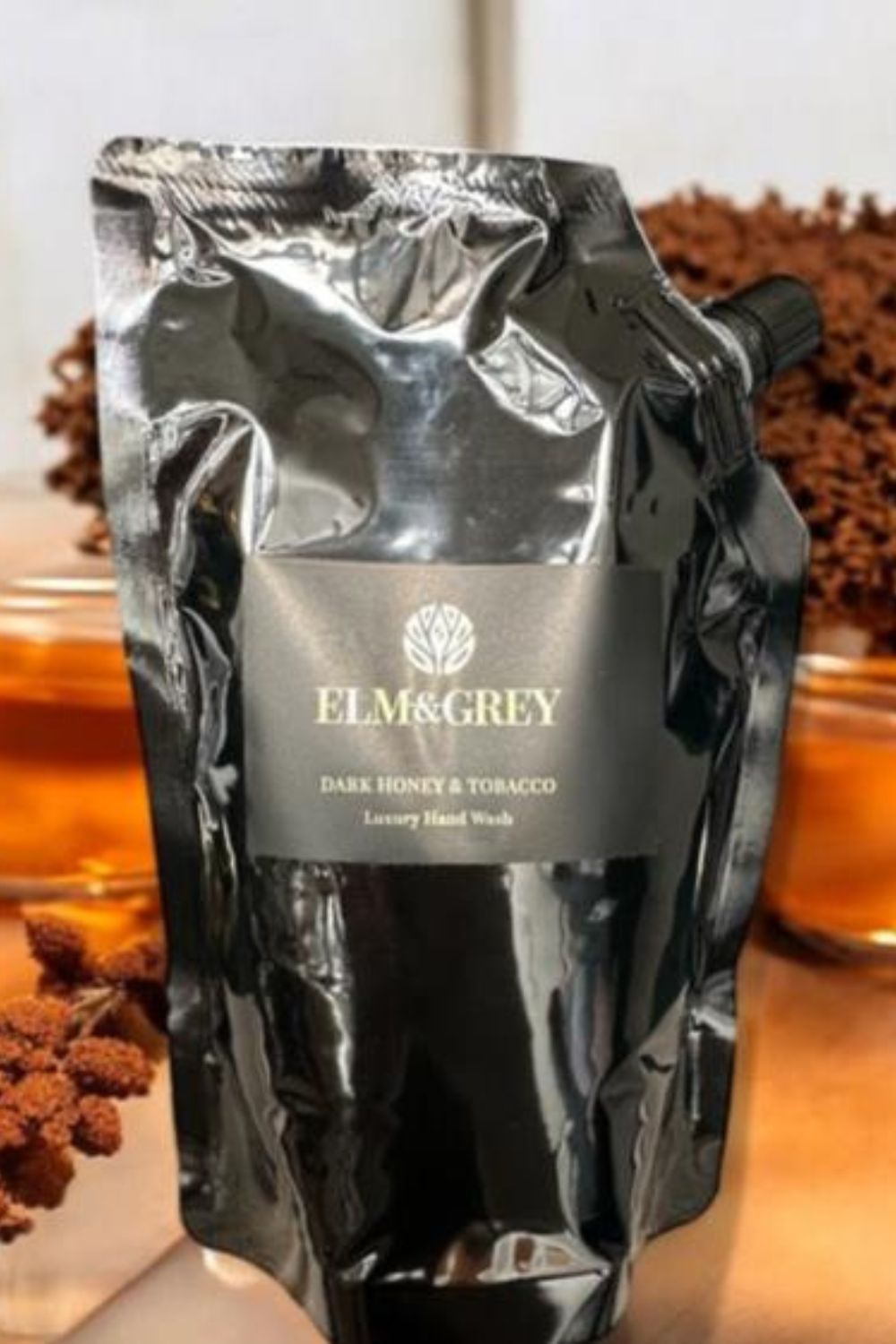 Black plum refill pouch wash of Elm & Grey Dark Honey & Tobacco soap on a wooden background