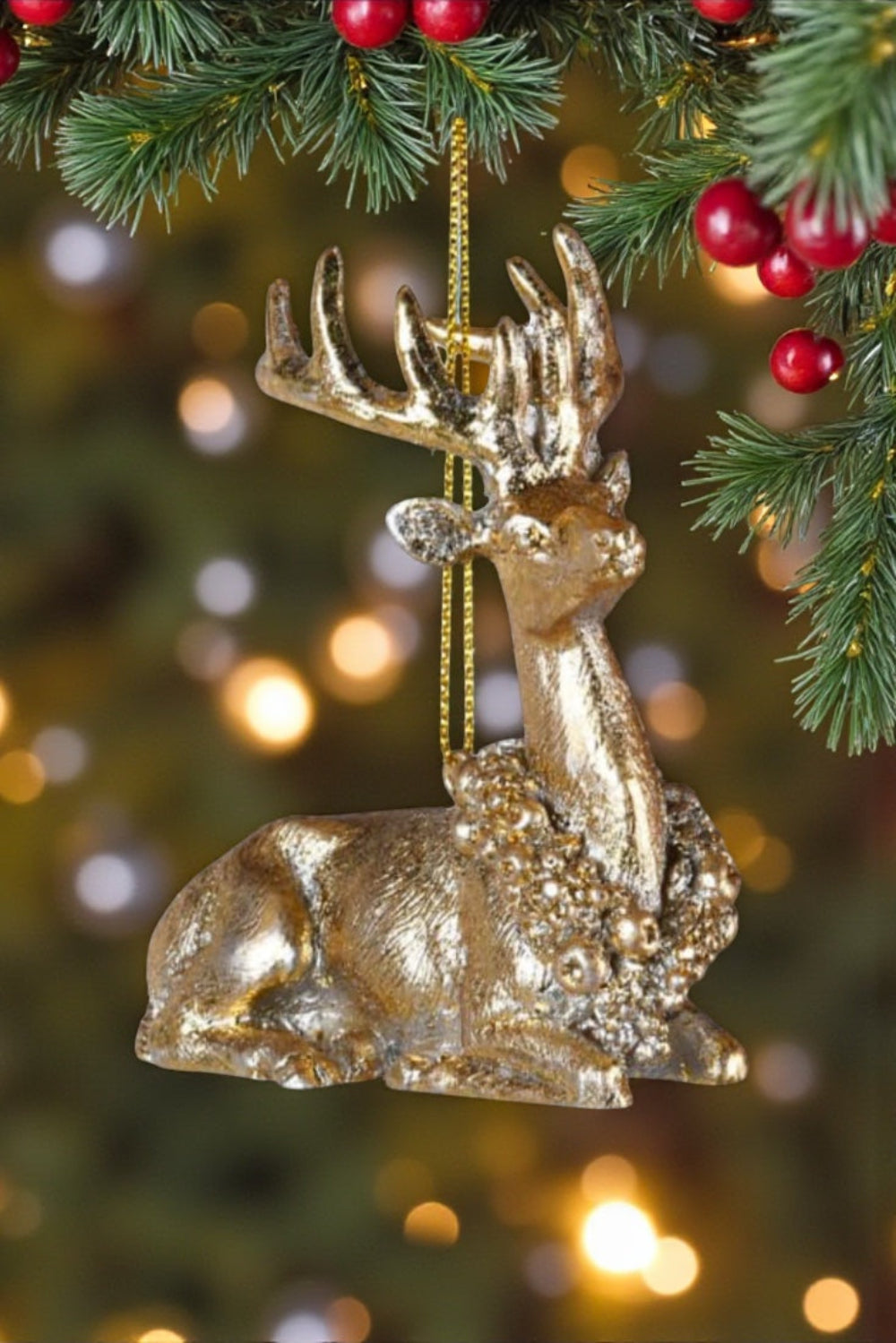 Gold deer ornament hanging on a Christmas tree with red berries and blurred lights in the background.