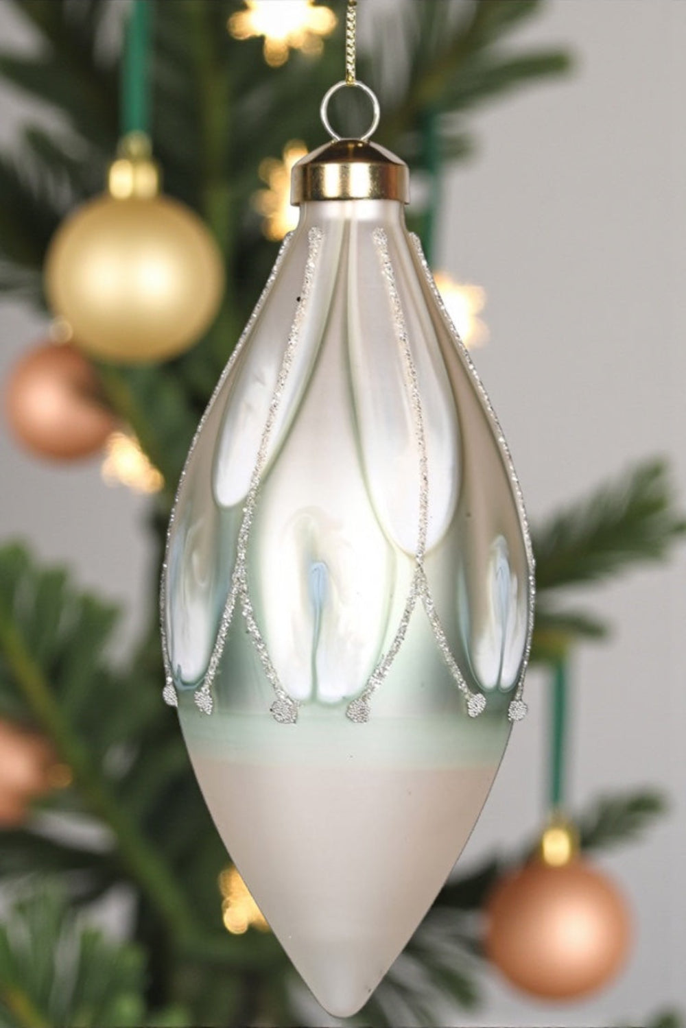 Decorative glass ornament hanging on a Christmas tree with blurred lights and greenery in the background.