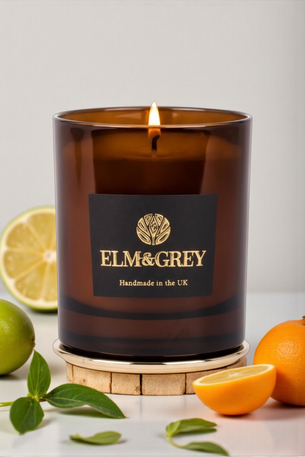 Brown Amber candle with Elm & Grey label surrounded by citrus fruits on a light background