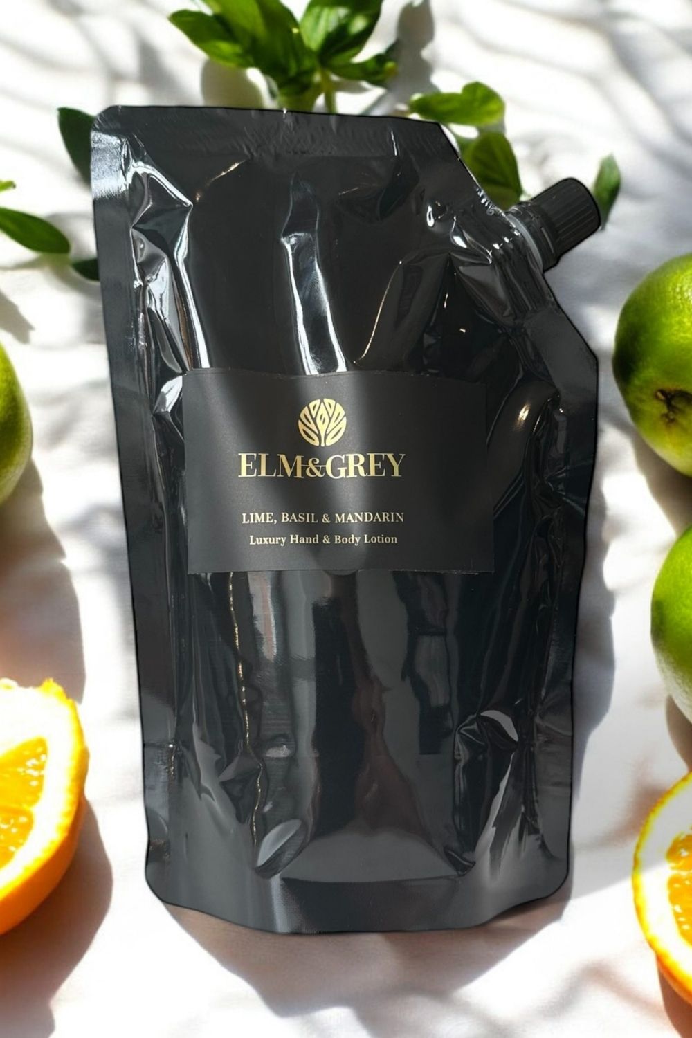 Black refill pouch with 'Elm & Grey' branding hand lotion on a white background with fruits.