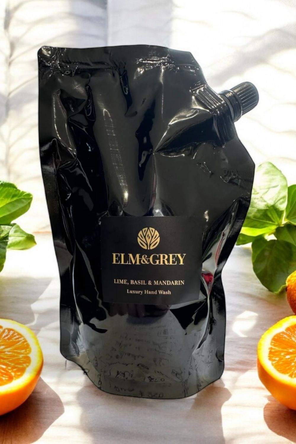Black packaging of Elm & Grey hand wash with oranges and leaves in the background