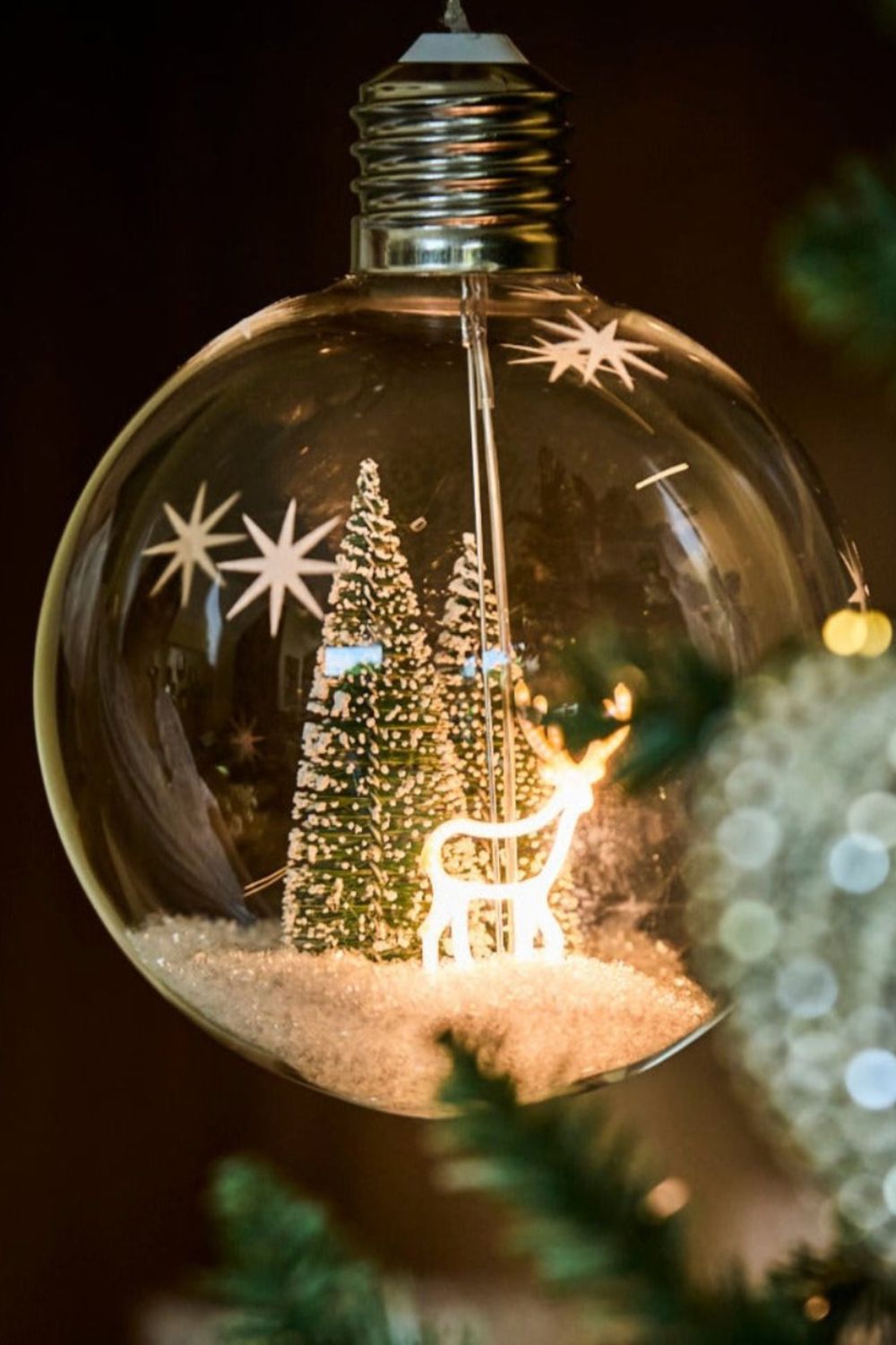 Decorative Christmas ornament shaped like a light bulb with a tree and reindeer inside.