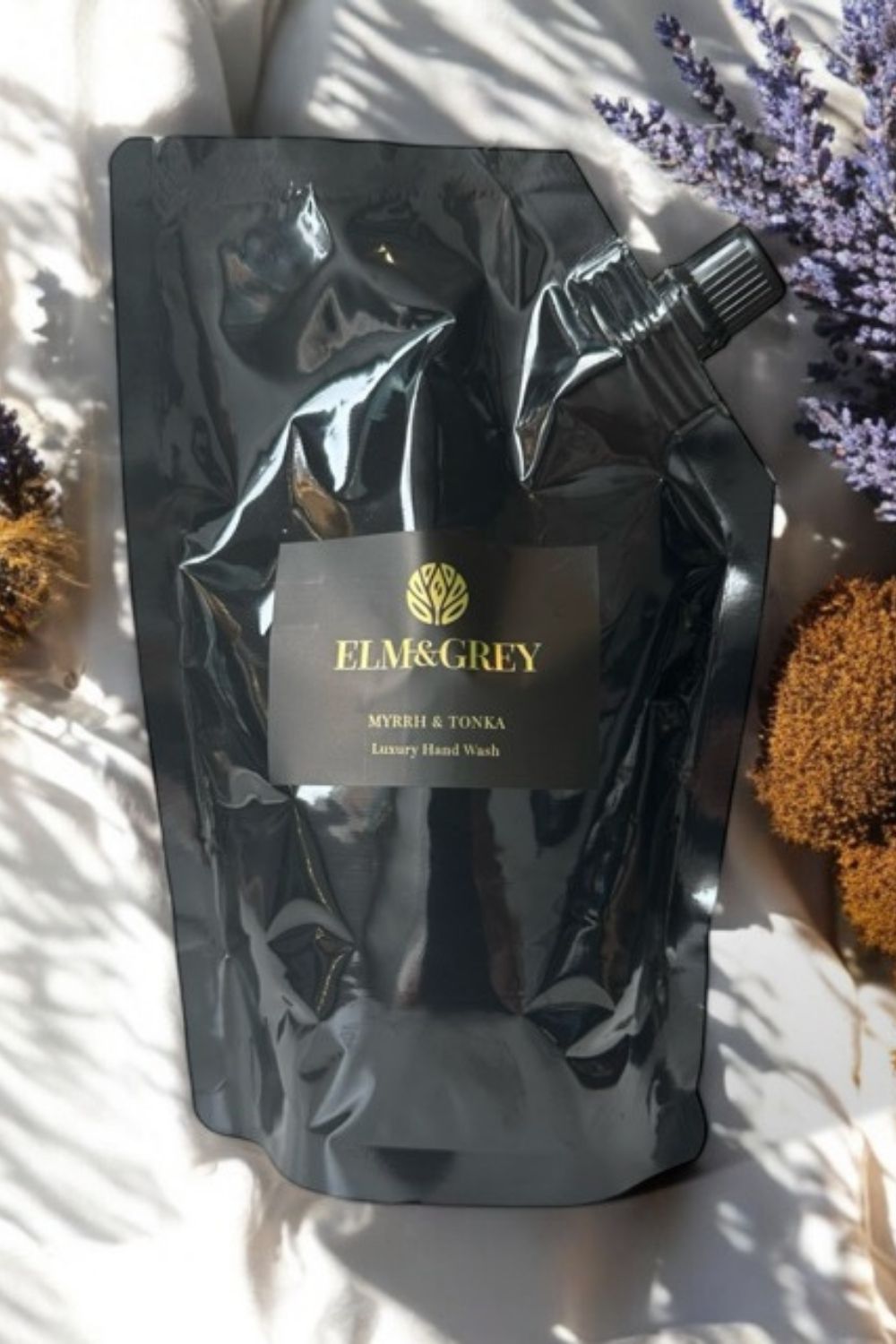 Black packaging of Elm & Grey hand wash on a light background with flowers.