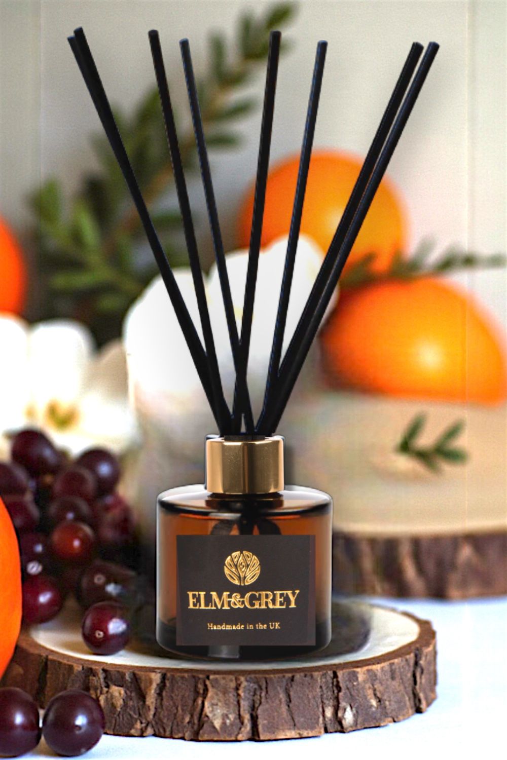 Reed diffuser with black sticks on a wooden coaster with fruits and leaves in the background