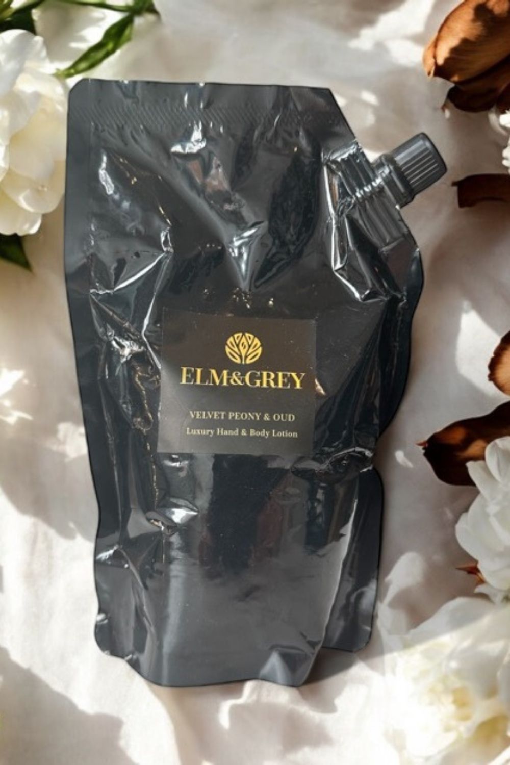 Black pouch of Elm & Grey body lotion on a white floral background