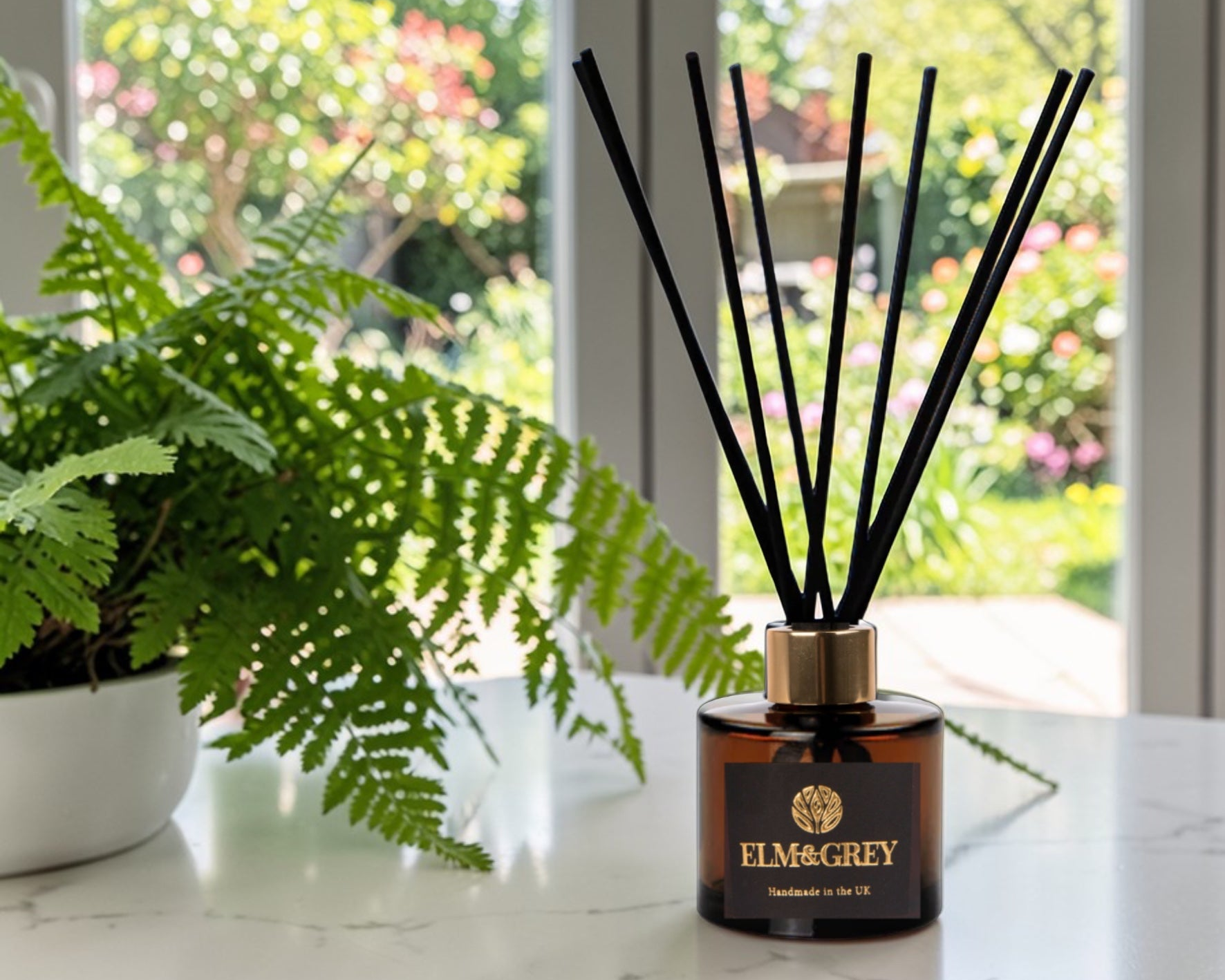 Elm & Grey diffuser on a table with a window and plants in the background