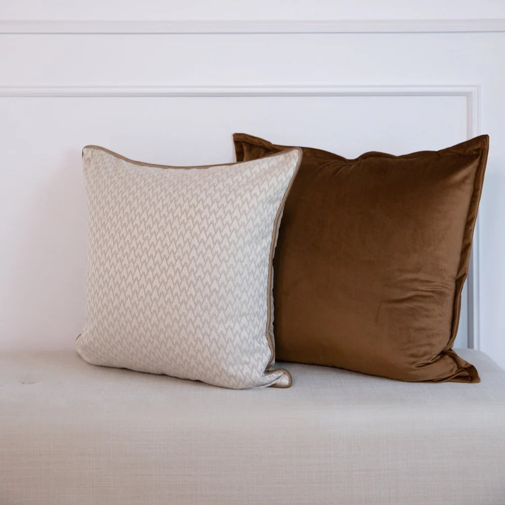 Two cushions, one beige and one brown, on a white surface.