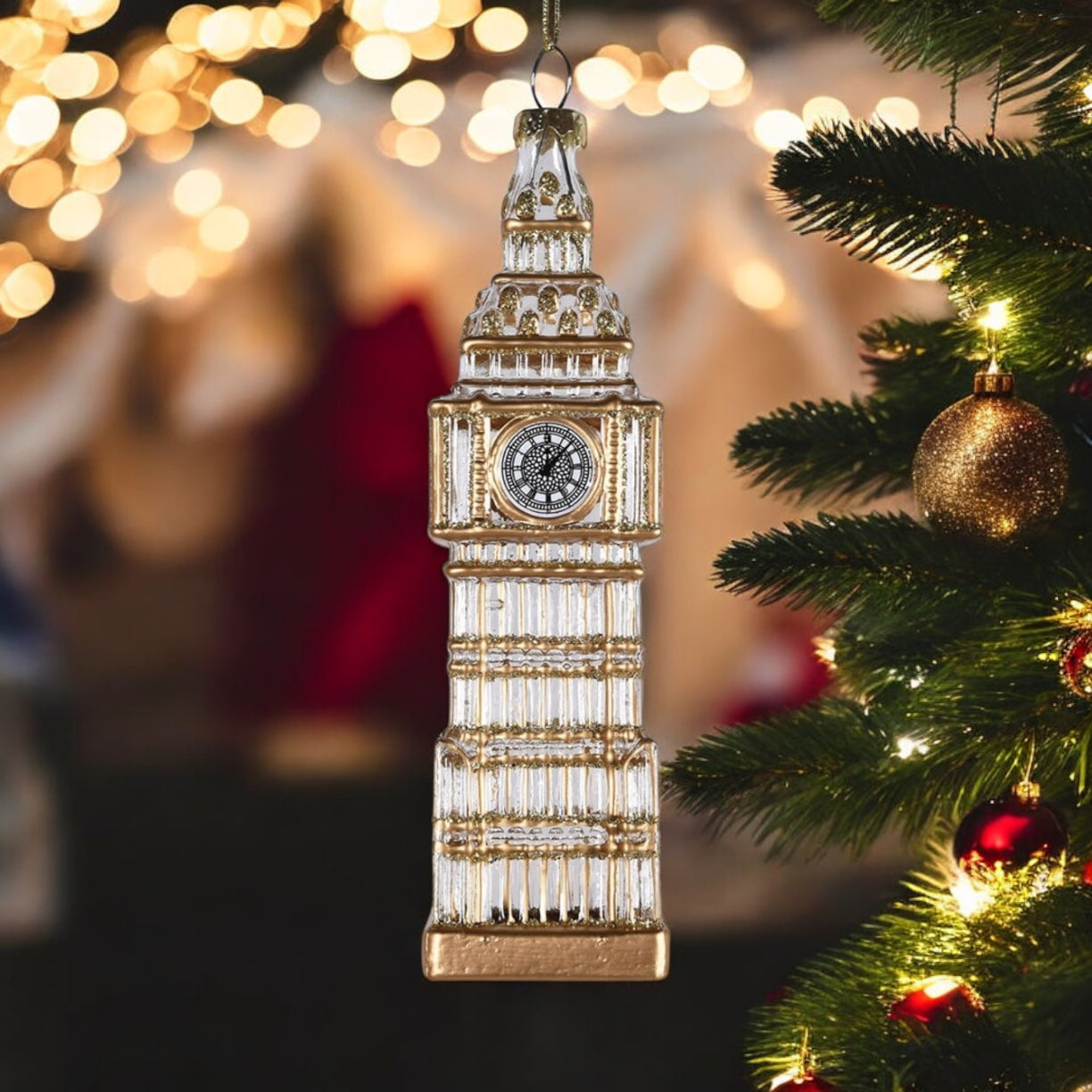 Decorative Big Ben clock tower ornament hanging on a Christmas tree with blurred lights in the background.