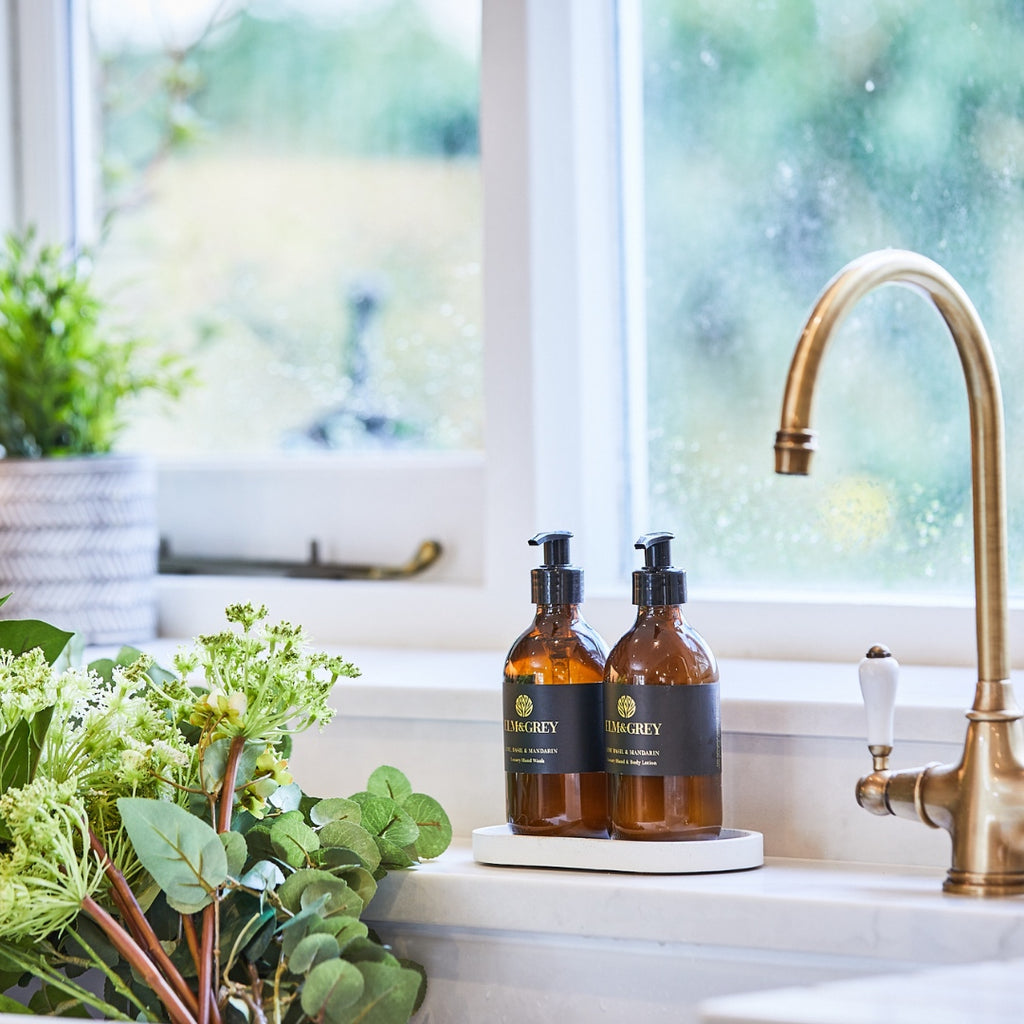 Elm and grey Amber Bottles on white concrete tray by a sink in a kitchen with a brass faucet