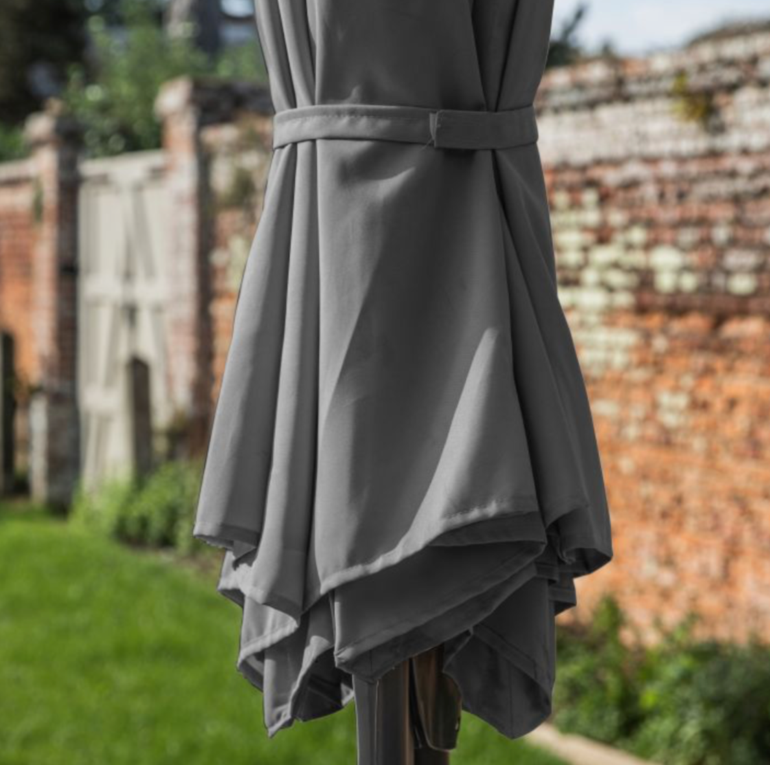 Gray umbrella with a belt against a brick wall and green grass background