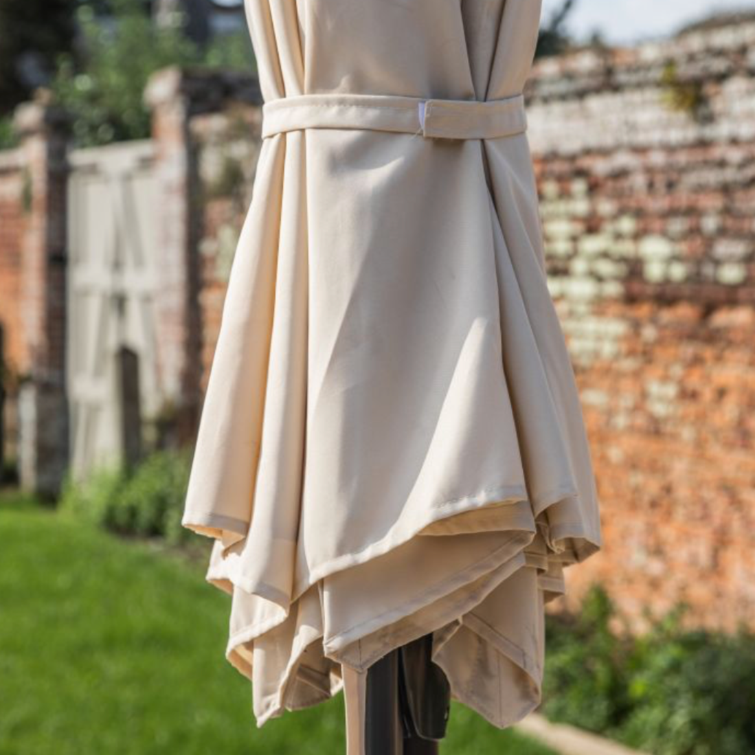 Beige outdoor umbrella with a brick wall and greenery in the background