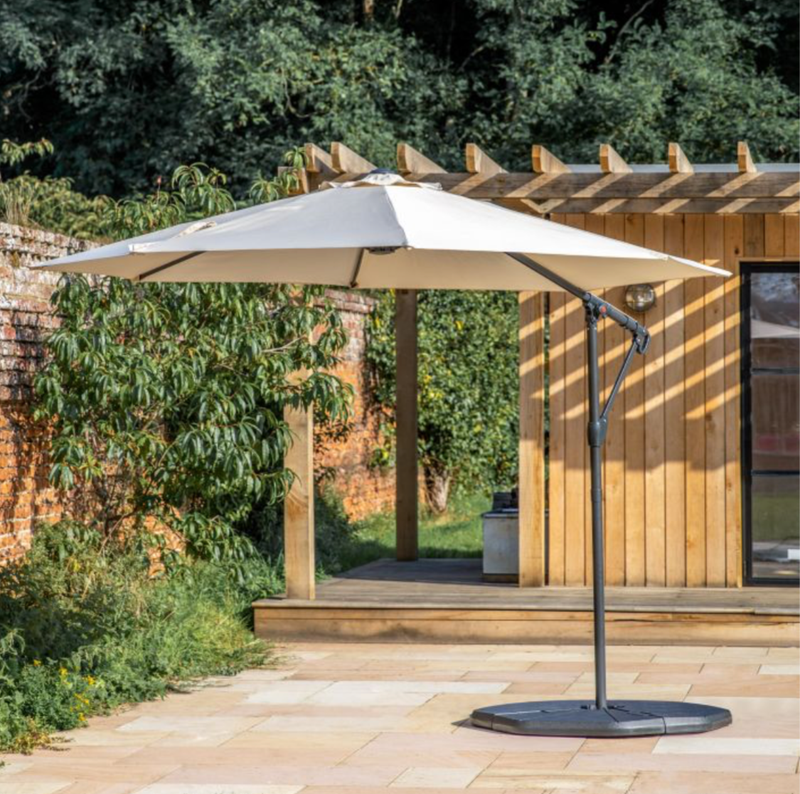 Beige patio umbrella on a stand in an outdoor setting with a wooden pergola and greenery.
